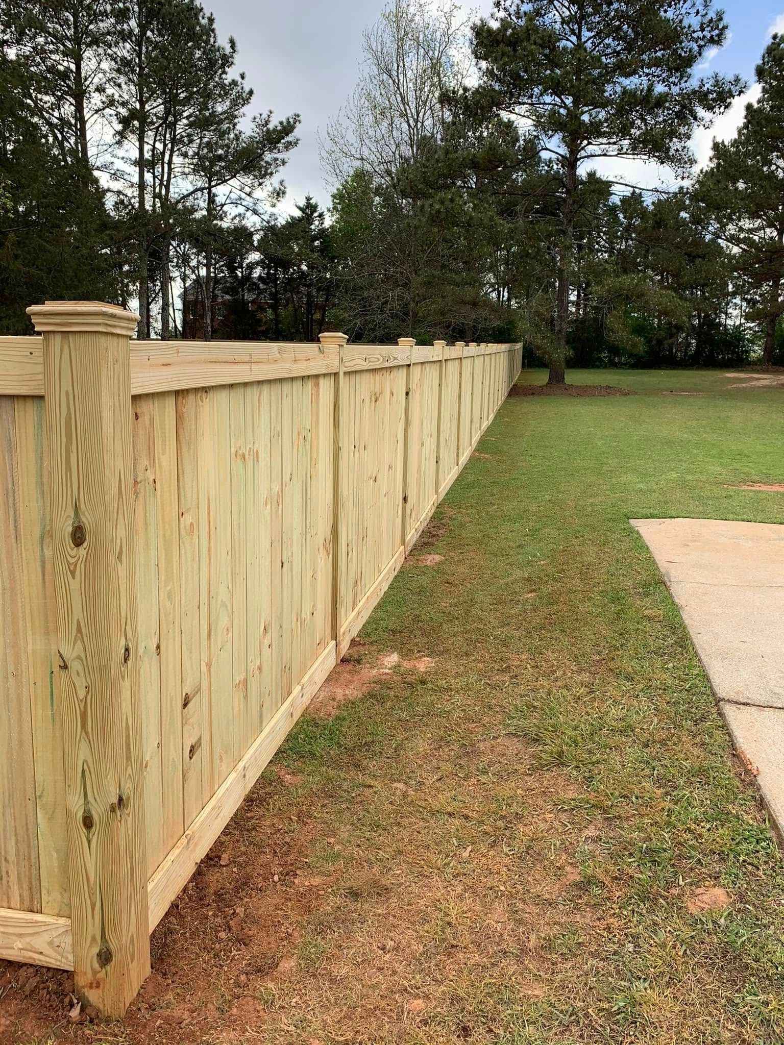 Wooden privacy fence beside a grassy yard with trees and a concrete patio.