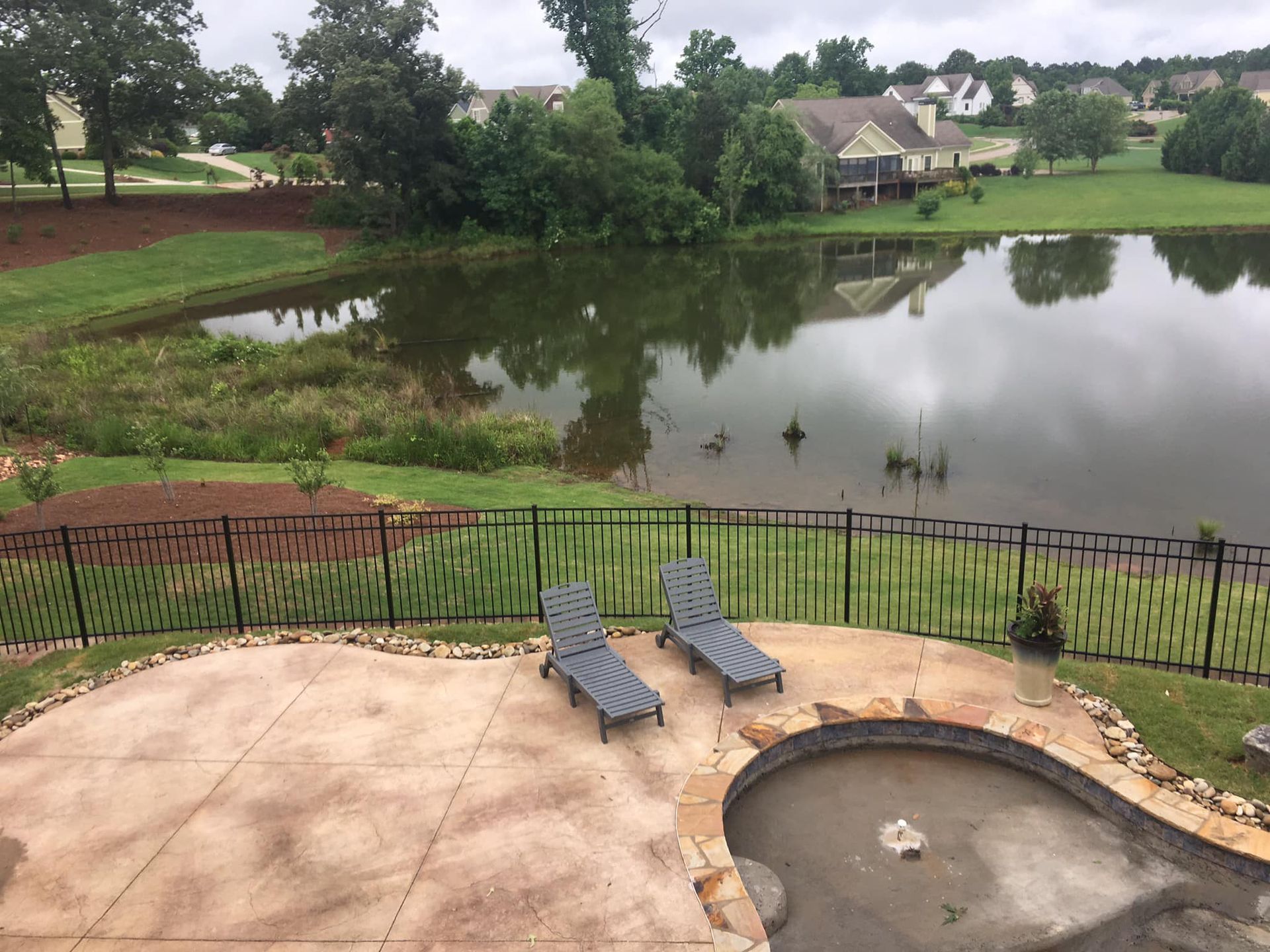 Patio with two lounge chairs and a fire pit overlooking a pond and grassy neighborhood.