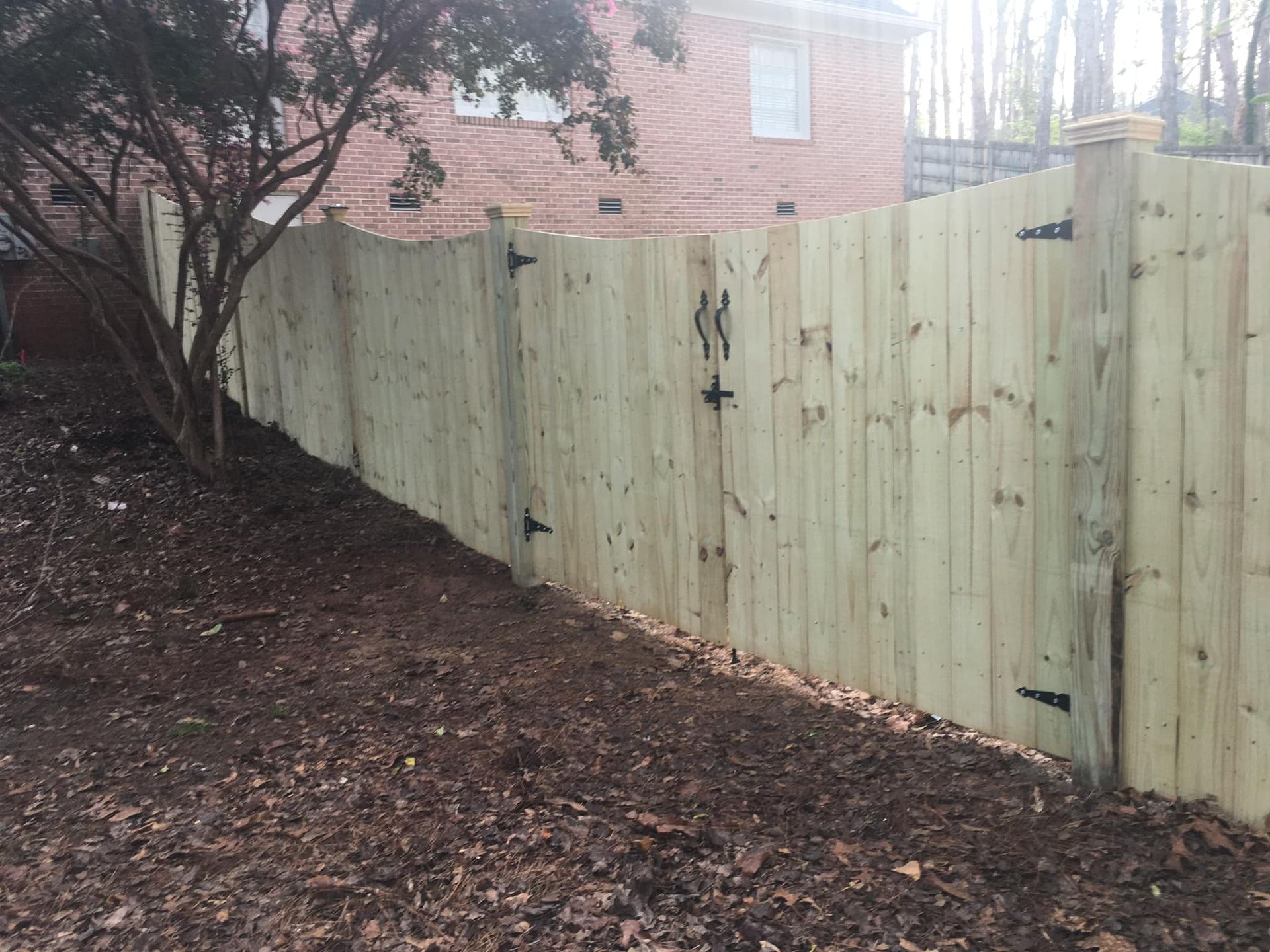 Fresh wooden fence along a leaf-covered slope beside a brick house and trees