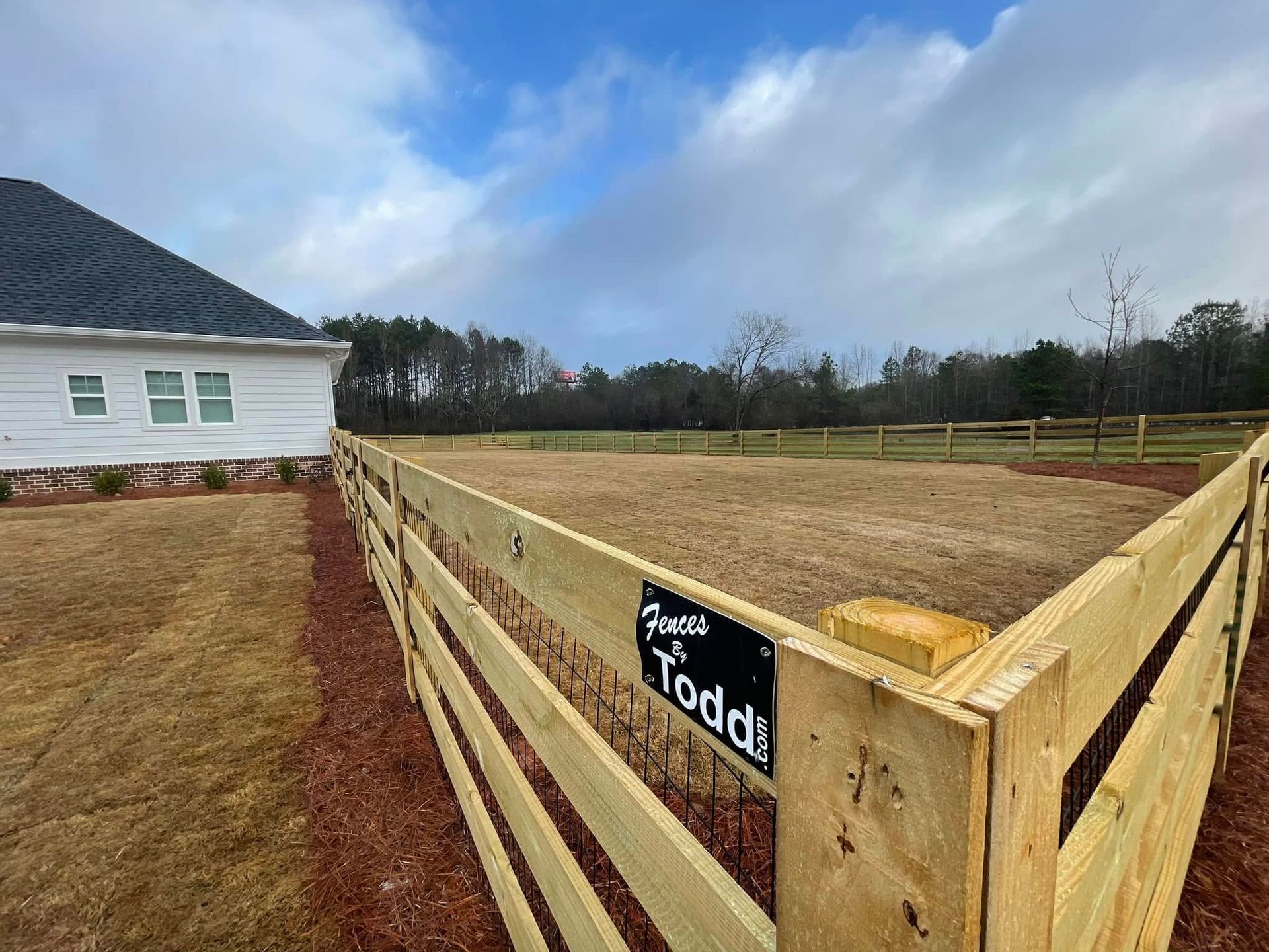 Wooden fenced paddock beside a white house under a cloudy sky