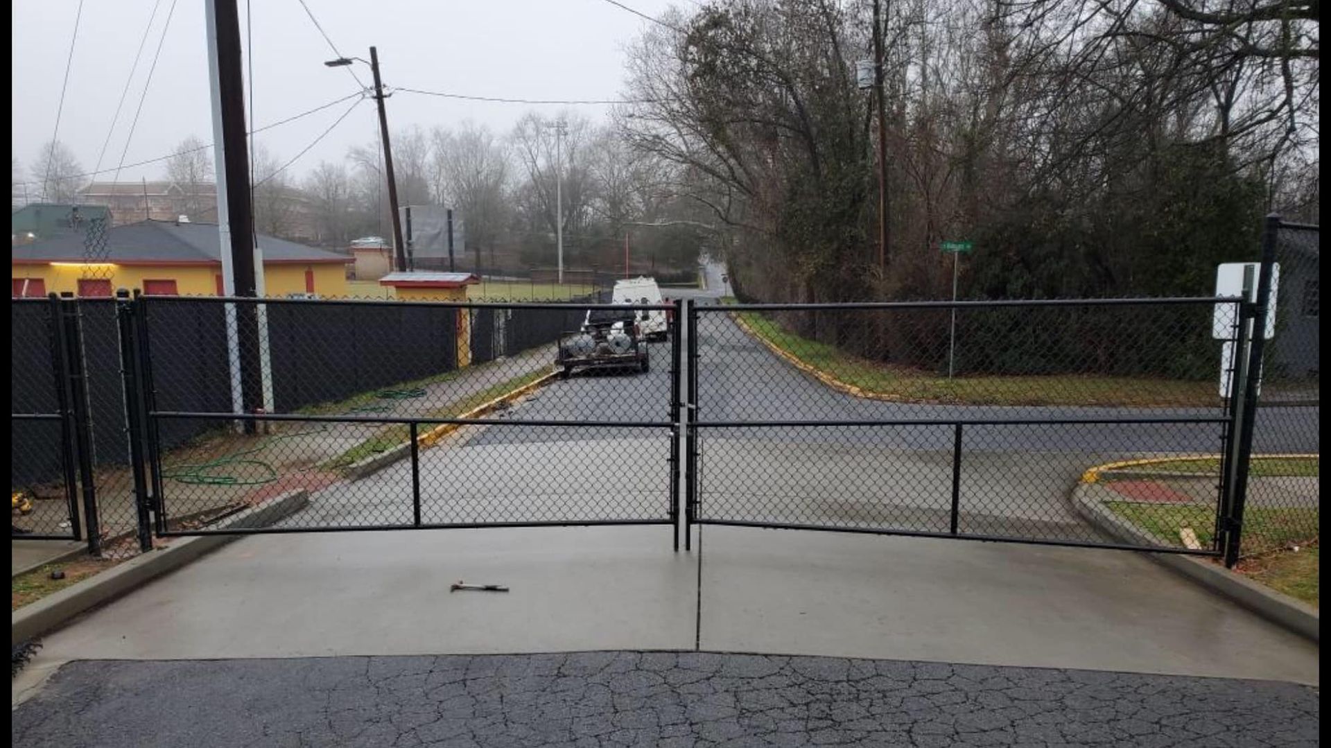 Closed chain-link gate across a wet road on a cloudy day, with a parked utility truck beyond it.