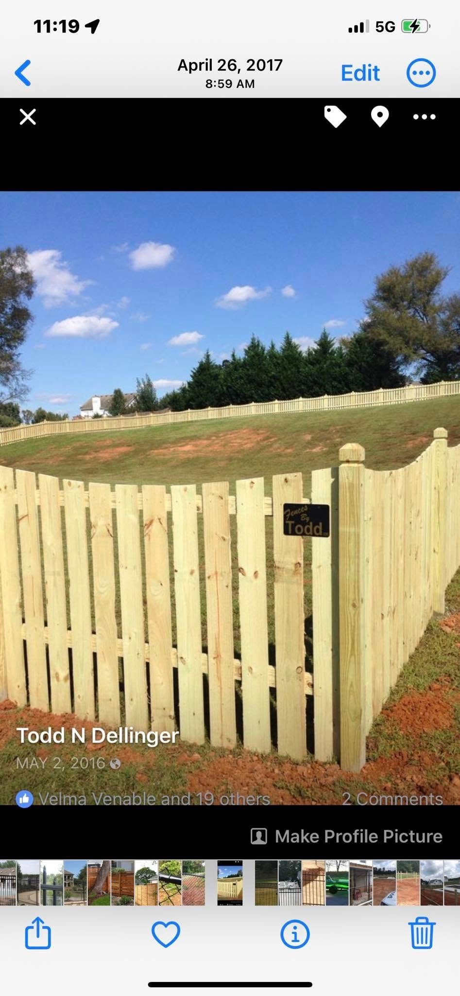 Wooden fence with a gate and sign in a grassy cemetery under a blue sky.