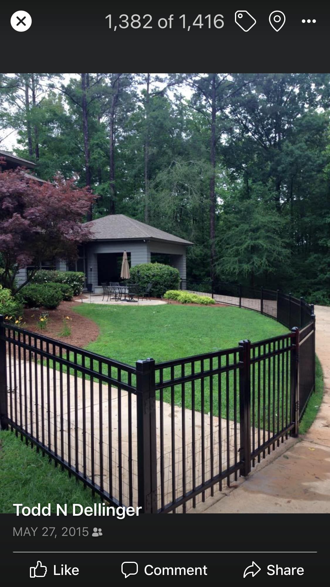 Black metal fence enclosing a grassy yard with a small house and trees in the background