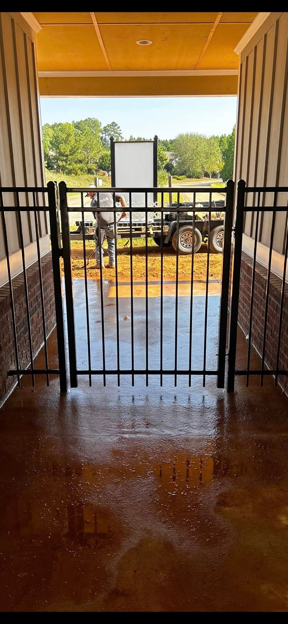 Covered balcony with black railing and wet floor overlooking trees and a parking area.