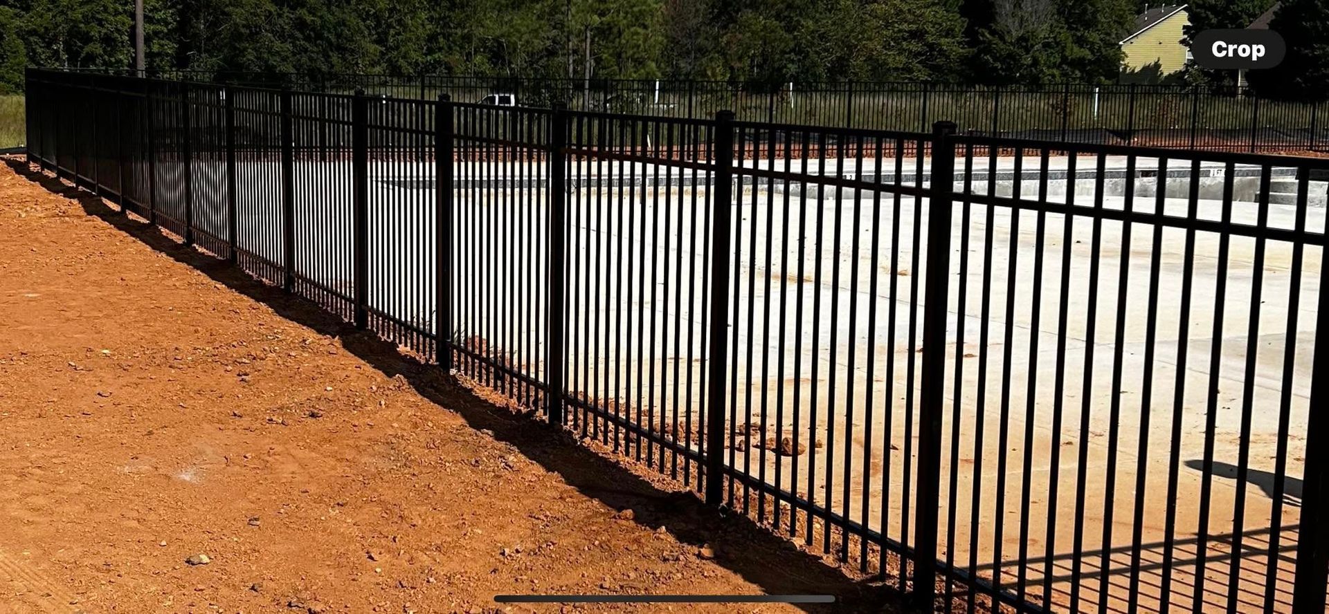 Black metal fence along a bright concrete court beside an orange dirt path and trees