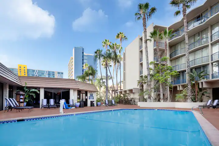 A large swimming pool in front of a hotel with palm trees.