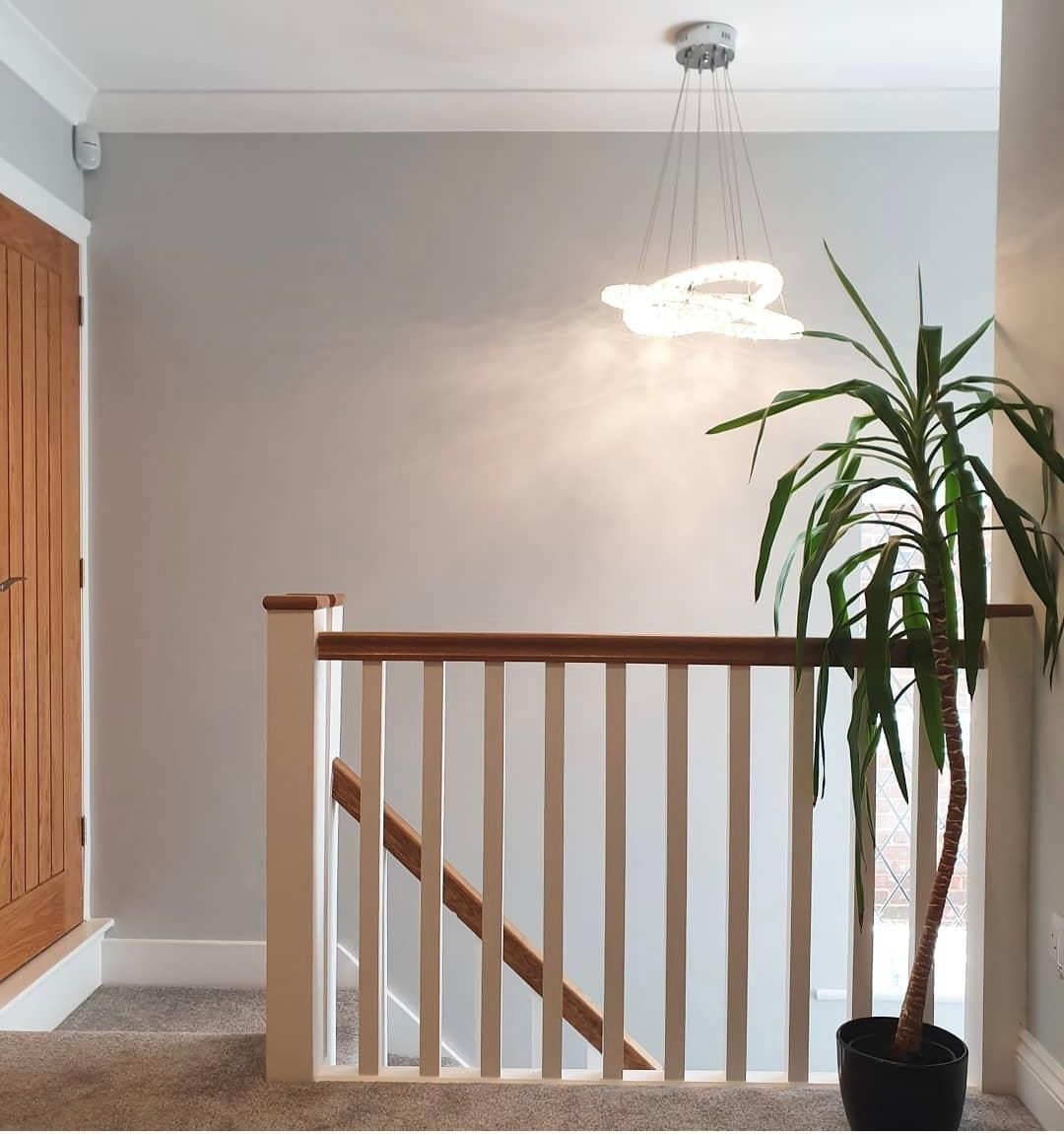 Hallway with stairs, a potted plant, and a modern light fixture. Neutral colors and a wood door.