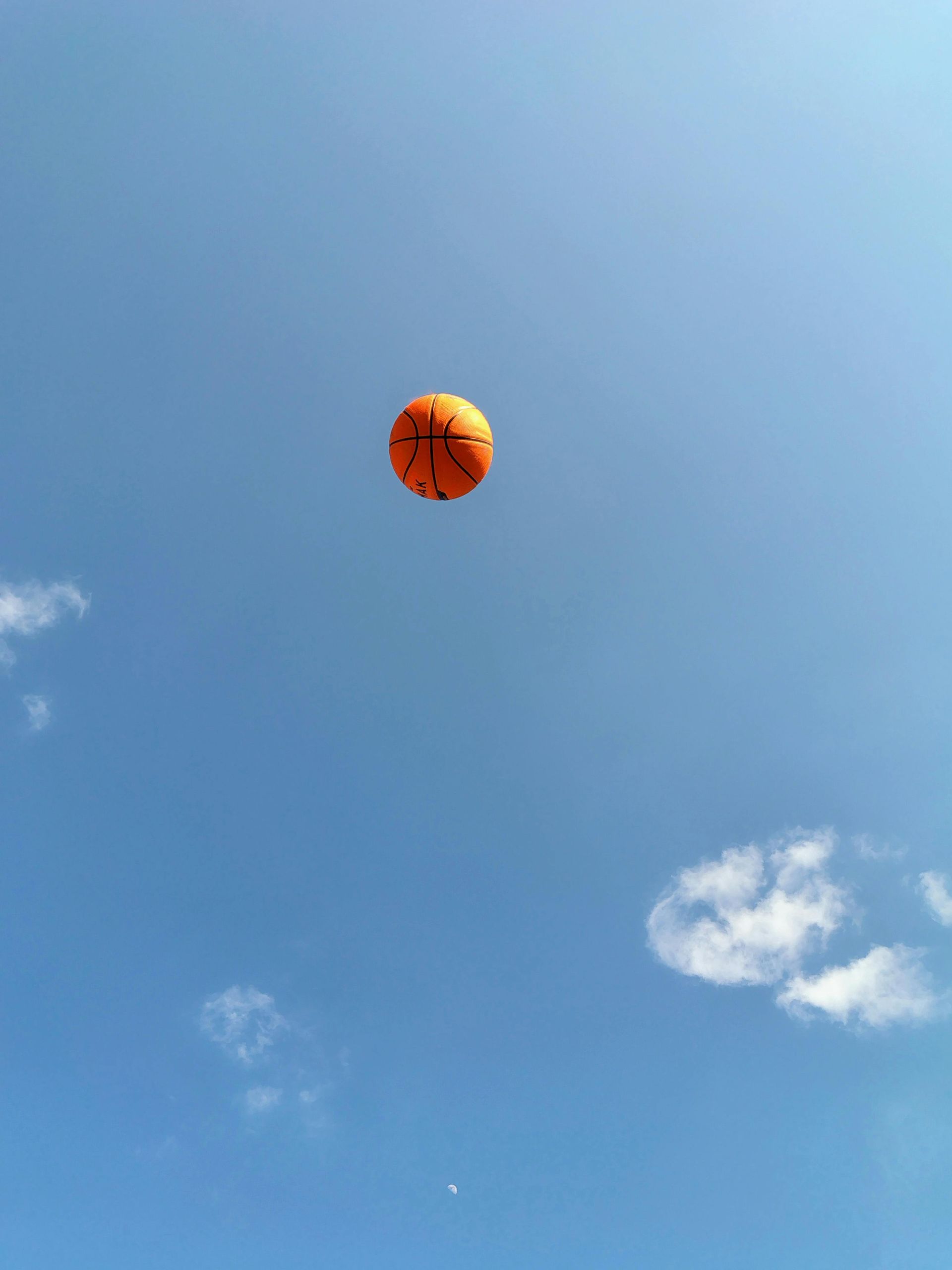 Orange ball floating in a clear blue sky with scattered white clouds.