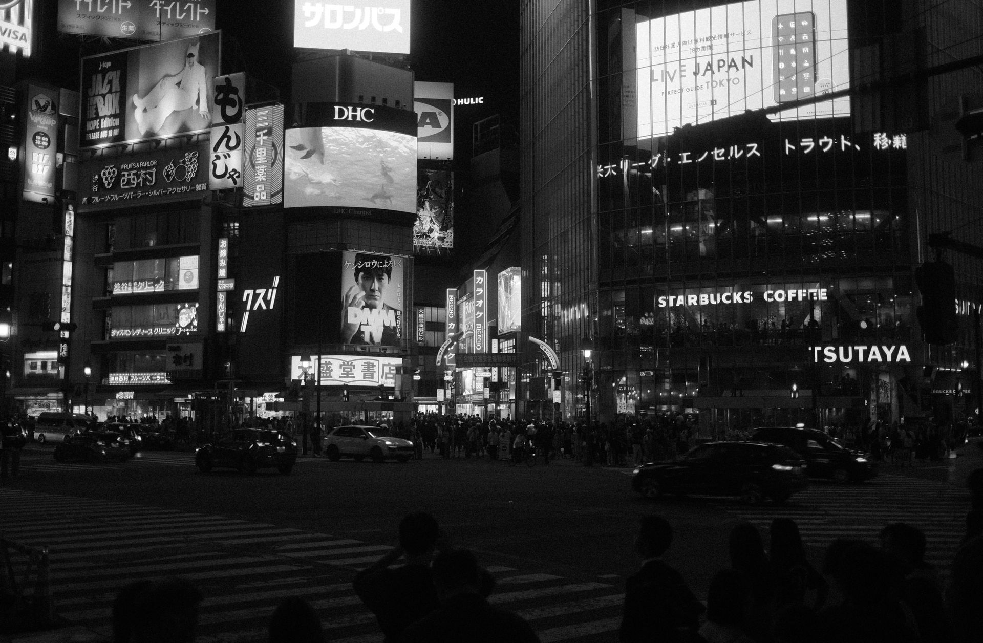 Nighttime view of Shibuya crossing in Tokyo, Japan. Neon signs illuminate buildings and busy streets.