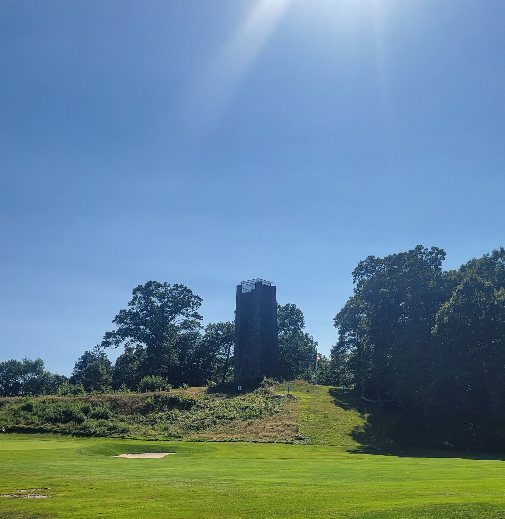 A golf course with a tower in the background on a sunny day.