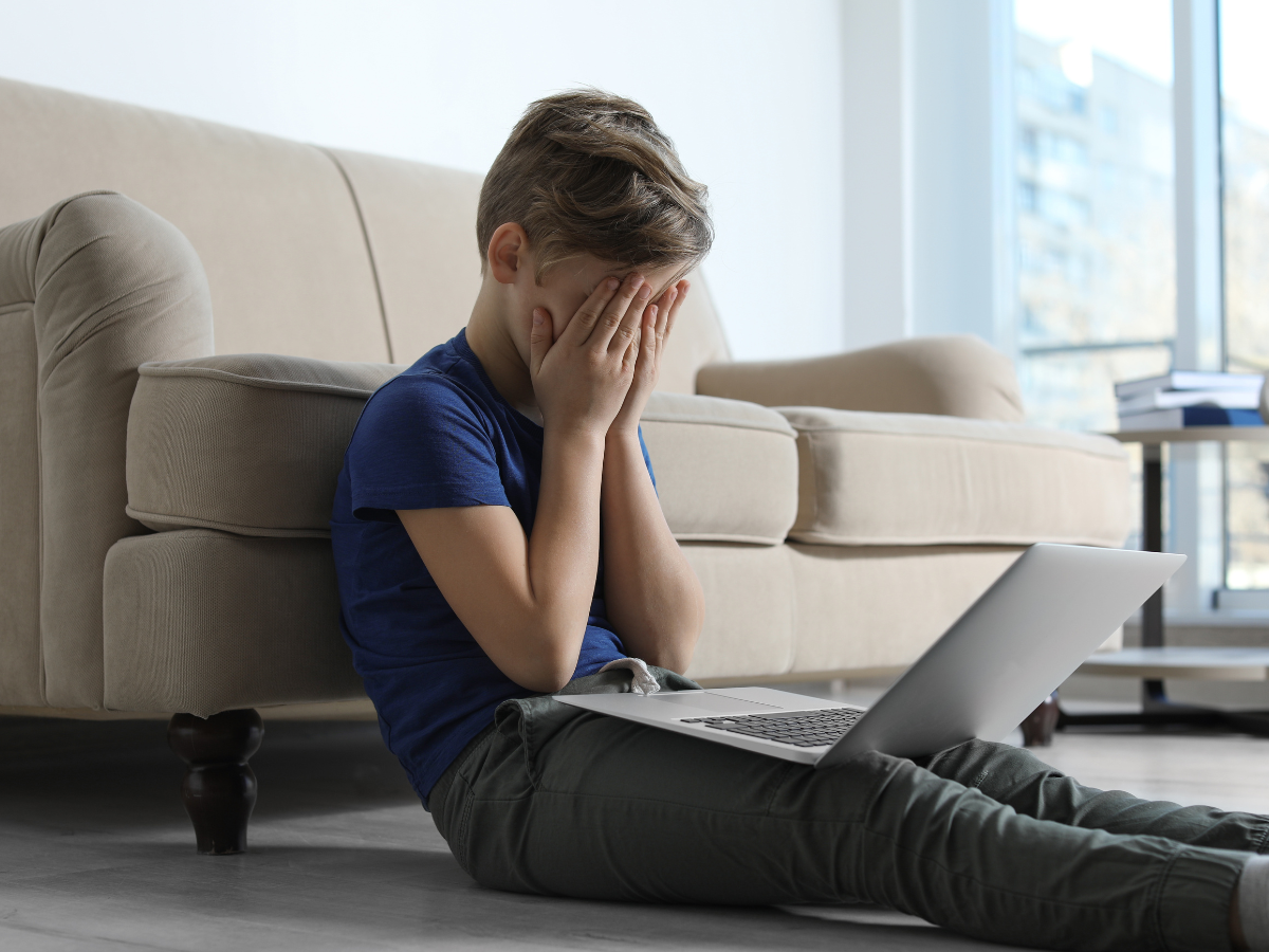 A young boy is sitting on the floor using a laptop computer.