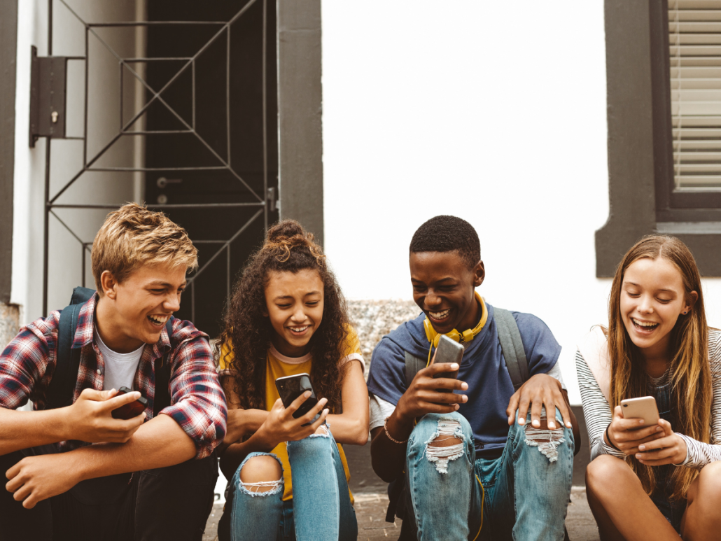 Hope Against Trafficking | Four teenagers sit outside a building, smiling and looking at their smartphones.