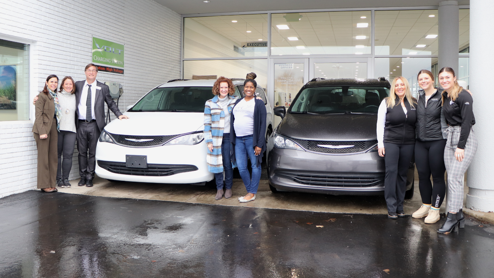 A group of people are standing in front of a car dealership.