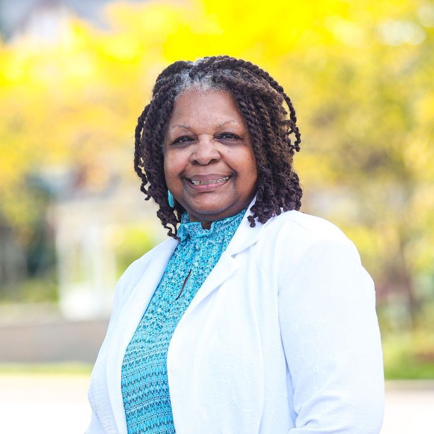 A woman wearing a white coat and a blue shirt is smiling for the camera.