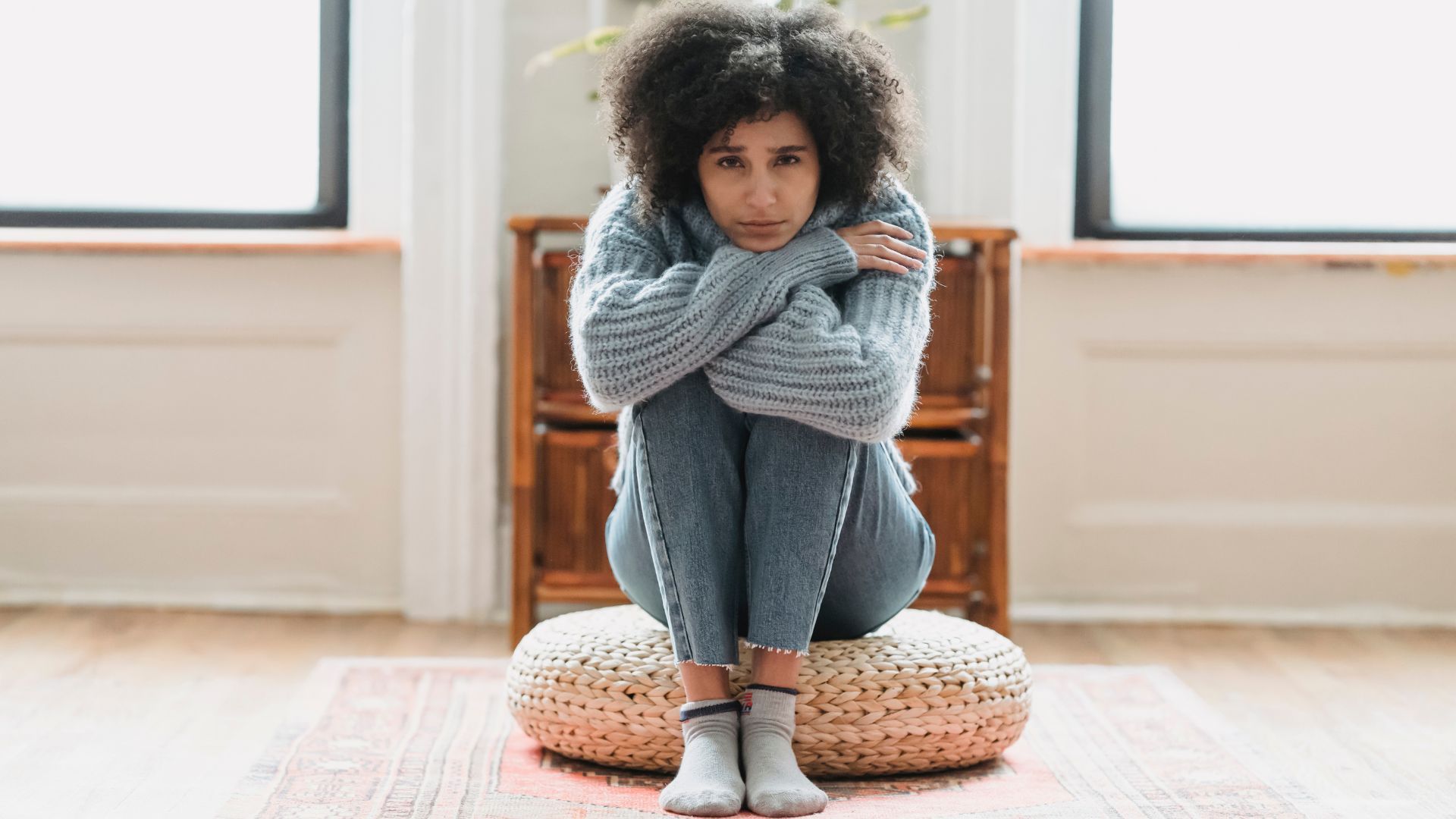 A woman is sitting on a pillow on the floor in a living room.