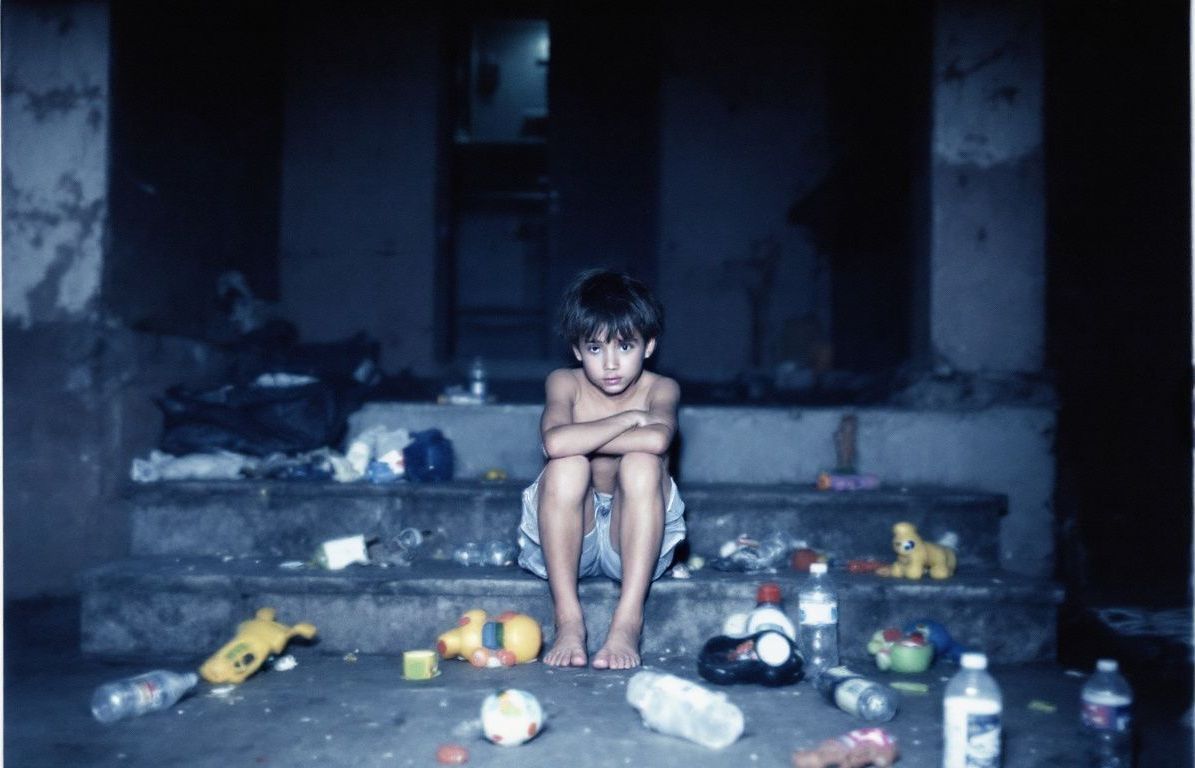 A boy sitting on the steps with trash all around him