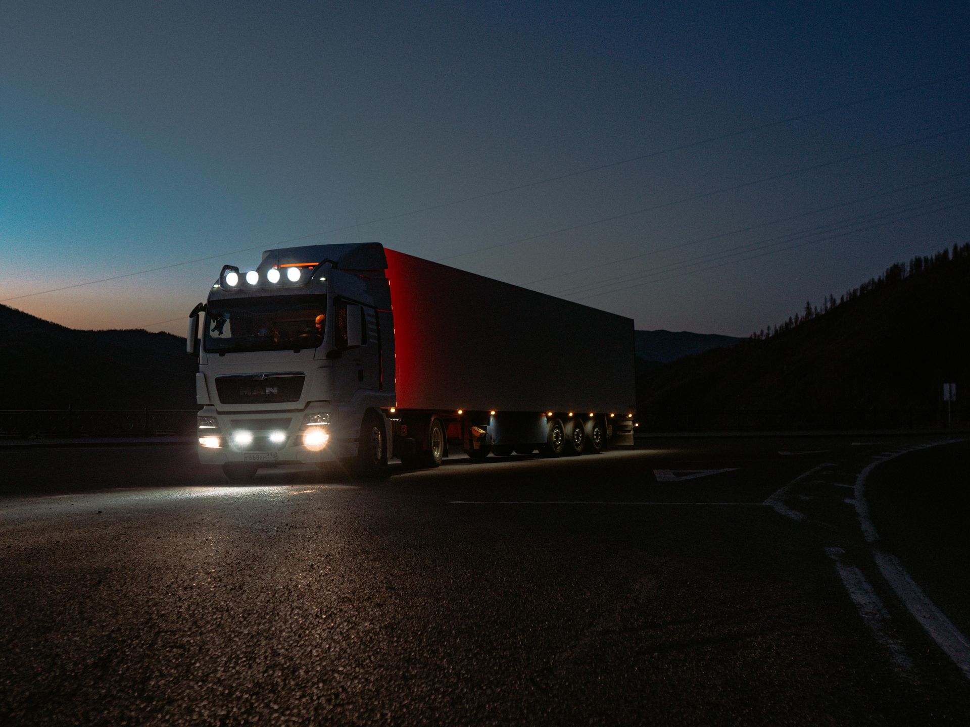 Truck driving on a road at dusk with headlights illuminating the asphalt.