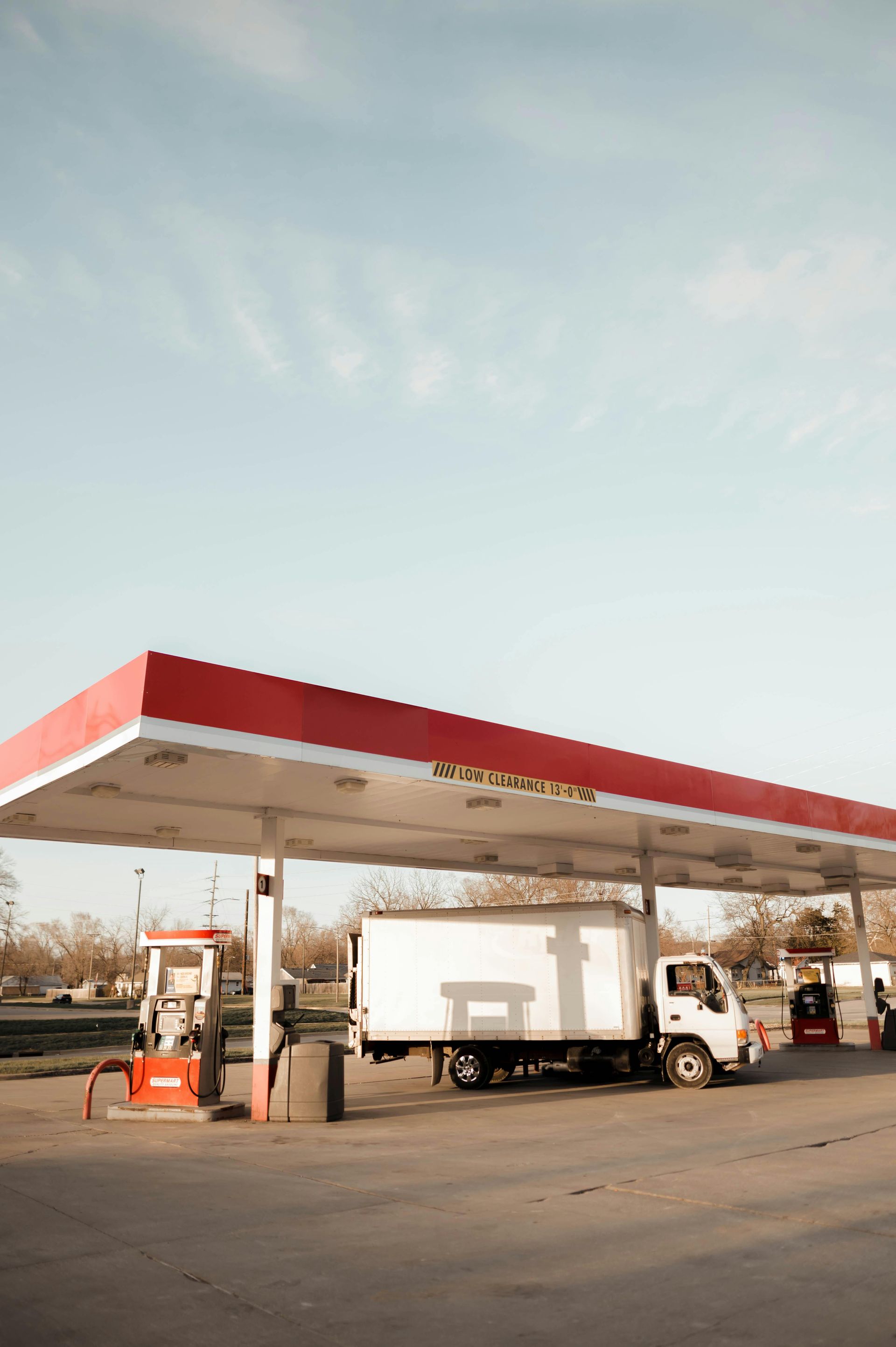 Truck parked under a red and white gas station canopy. A clear, blue sky is overhead.