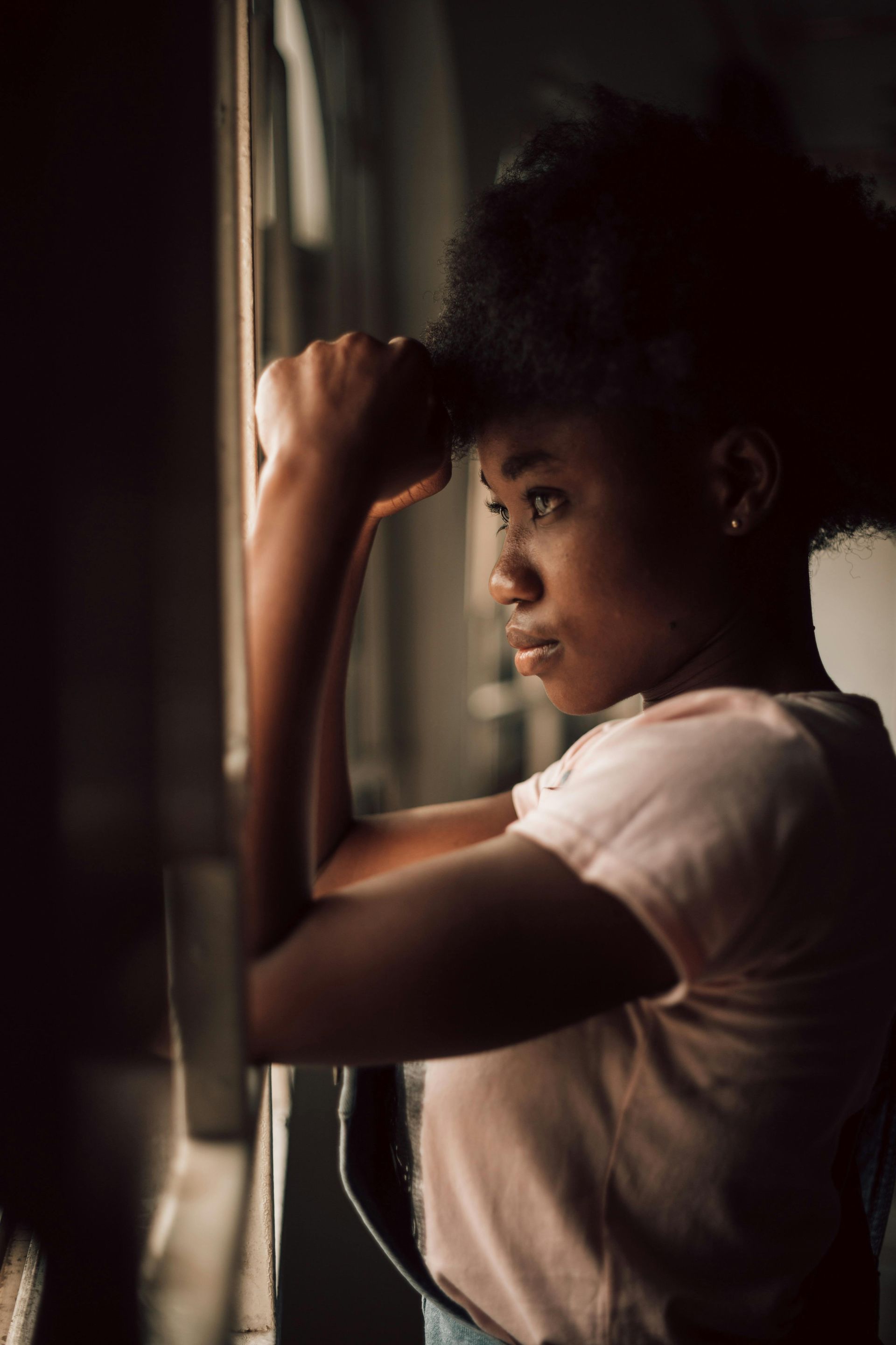 Person standing by a window, resting an arm on the frame and gazing outside in soft light