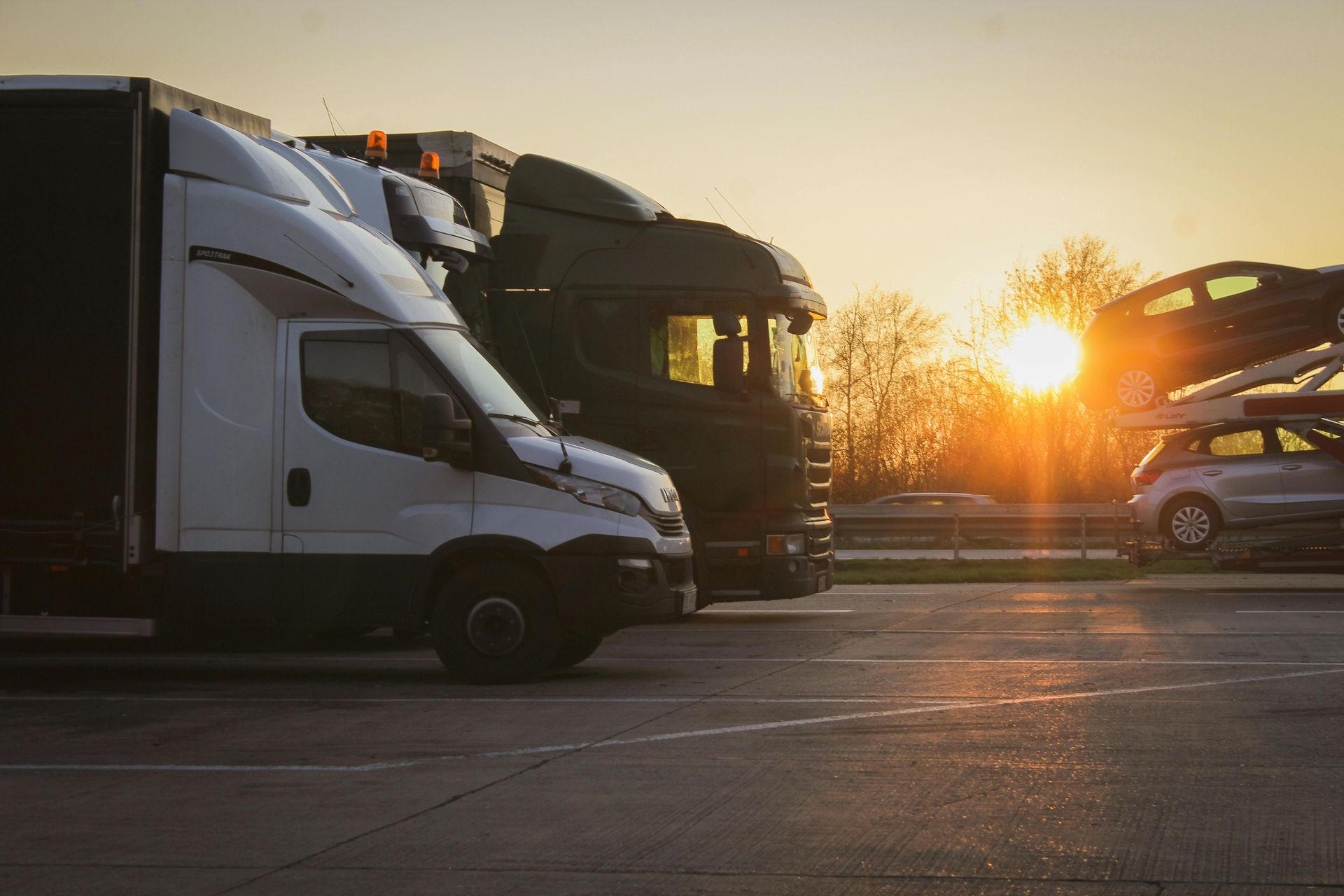 Trucks parked at dusk, sun setting behind them on a paved lot.