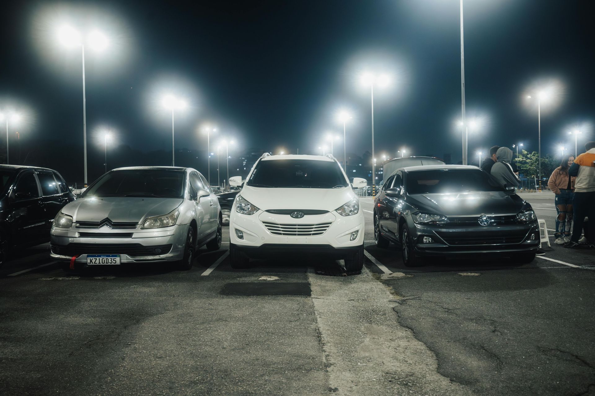 Cars parked in a dimly lit parking lot at night; streetlights are on.