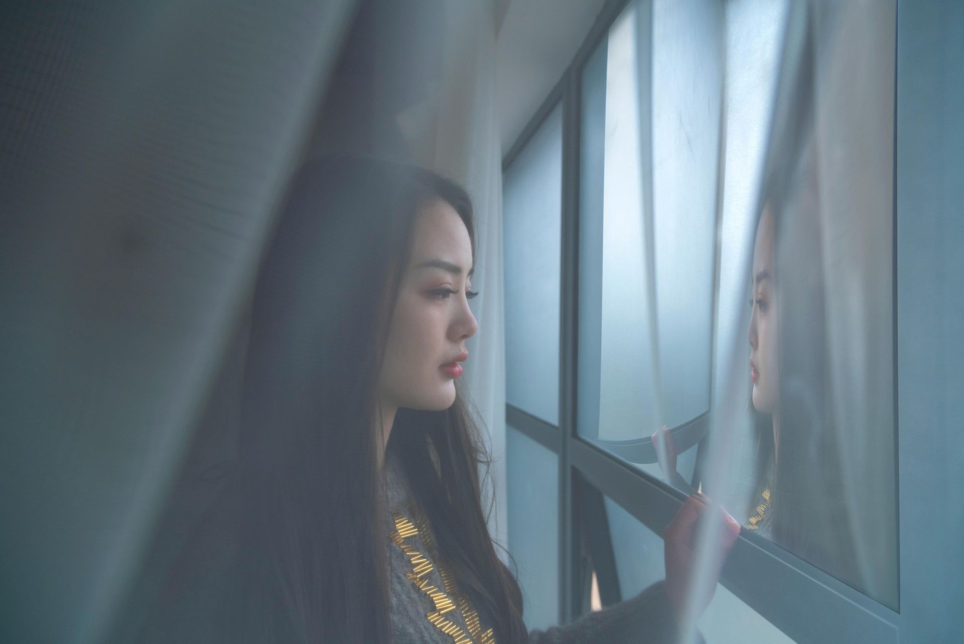 Woman gazing out a frosted window in a dim, blue-toned room