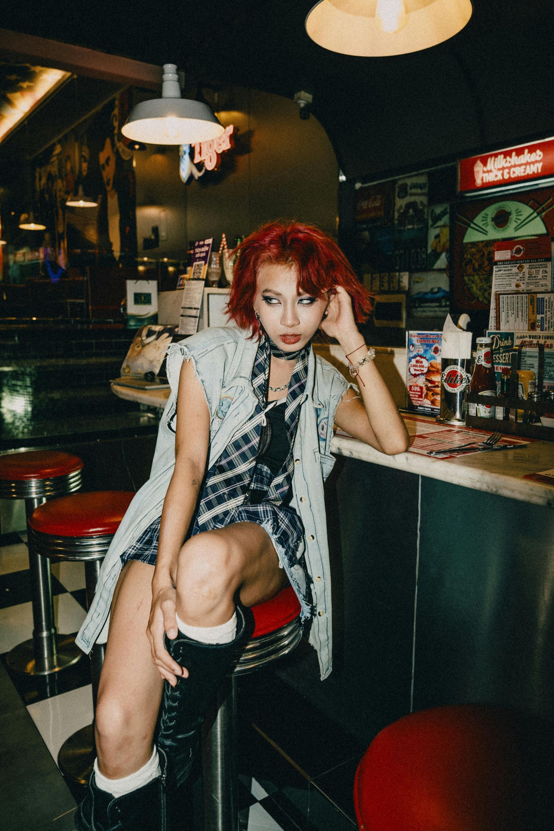 A woman with red hair is sitting on a bar stool in a diner.