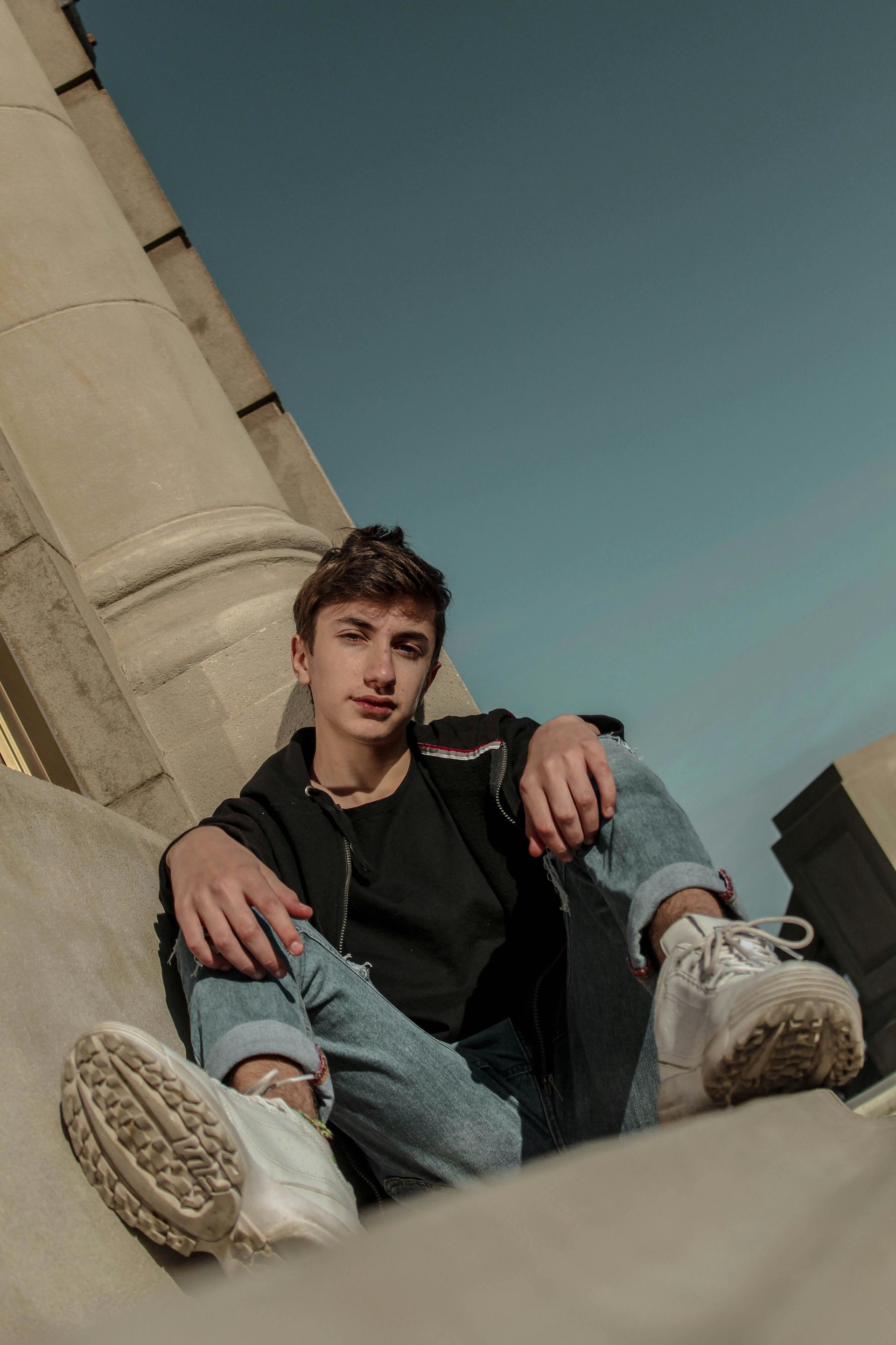 A young man is sitting on the ground with his legs crossed.