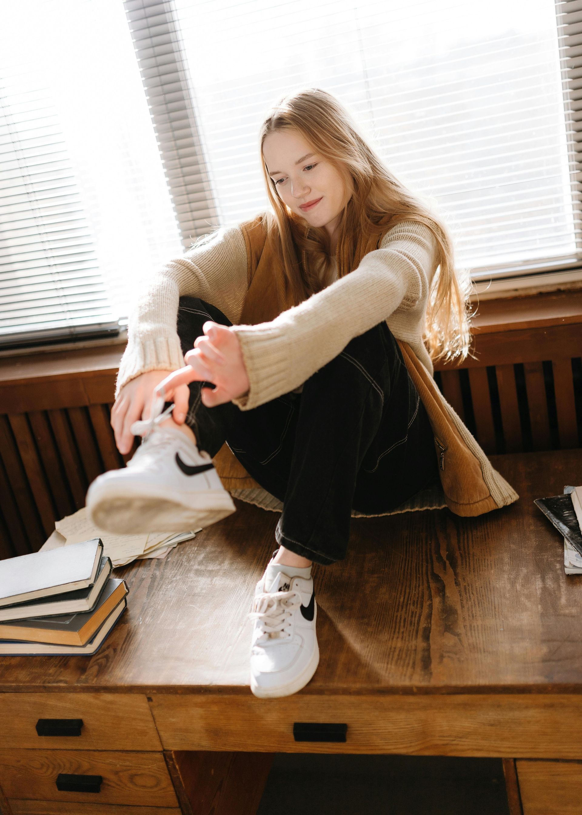 A woman is sitting on a desk tying her shoes.