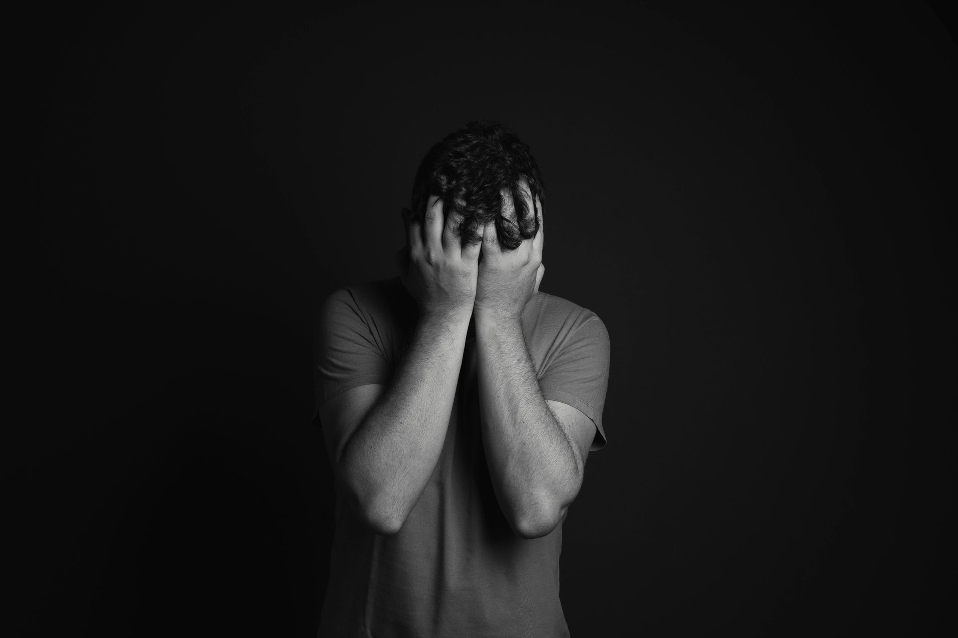 A man is covering his face with his hands in a black and white photo.