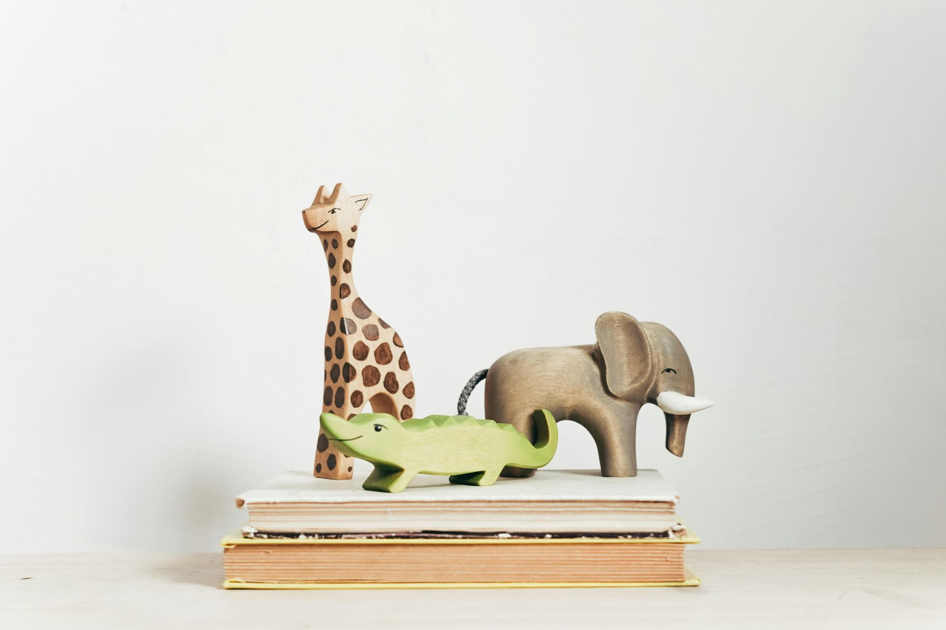 A giraffe , elephant , and crocodile are sitting on top of a stack of books.