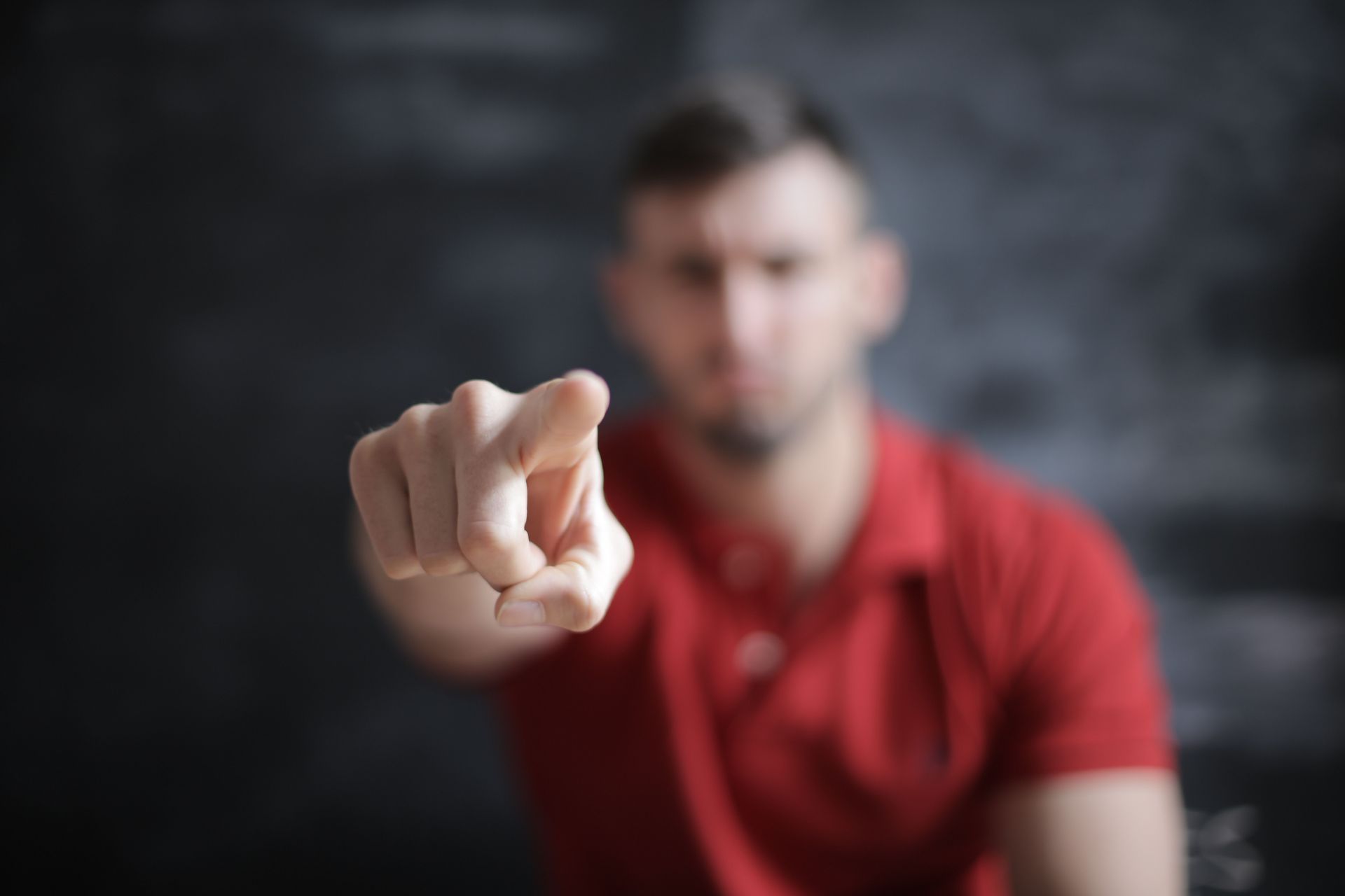 Man in a red shirt pointing toward the camera against a dark blurred background