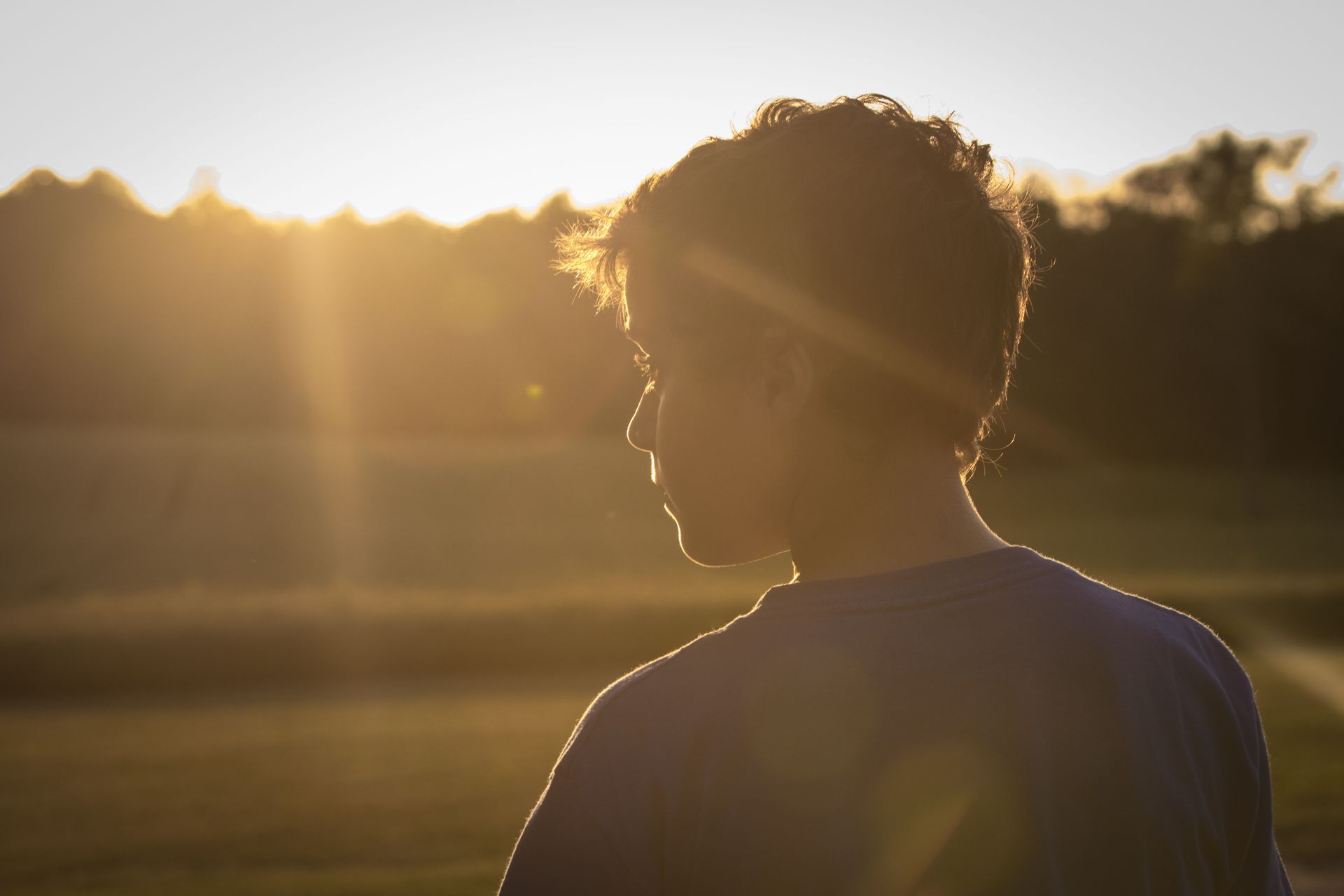 Backlit child in profile at sunset, with warm sunlight and trees in the background