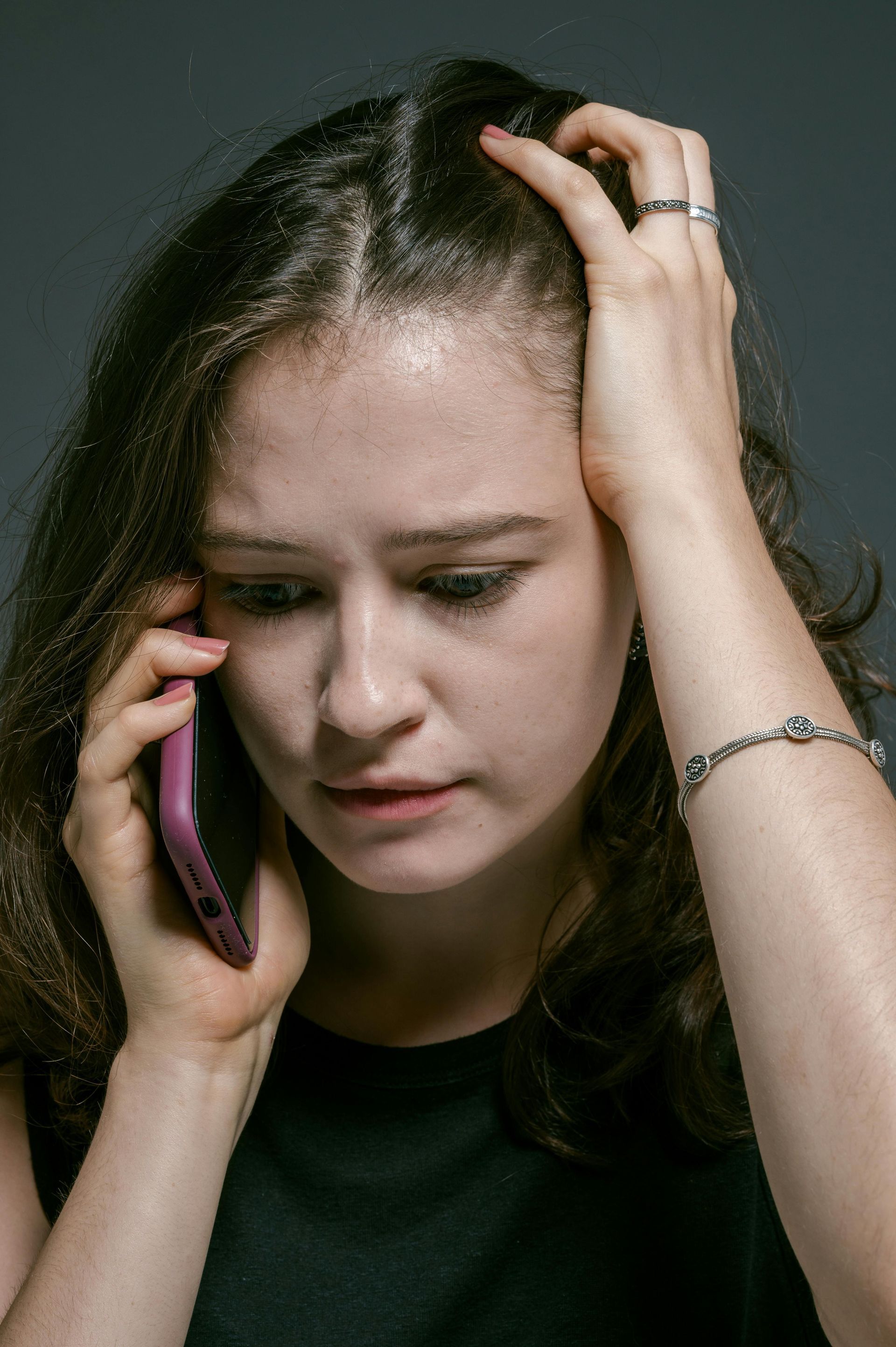 Woman holding her head while talking on a pink phone, looking stressed against a dark background