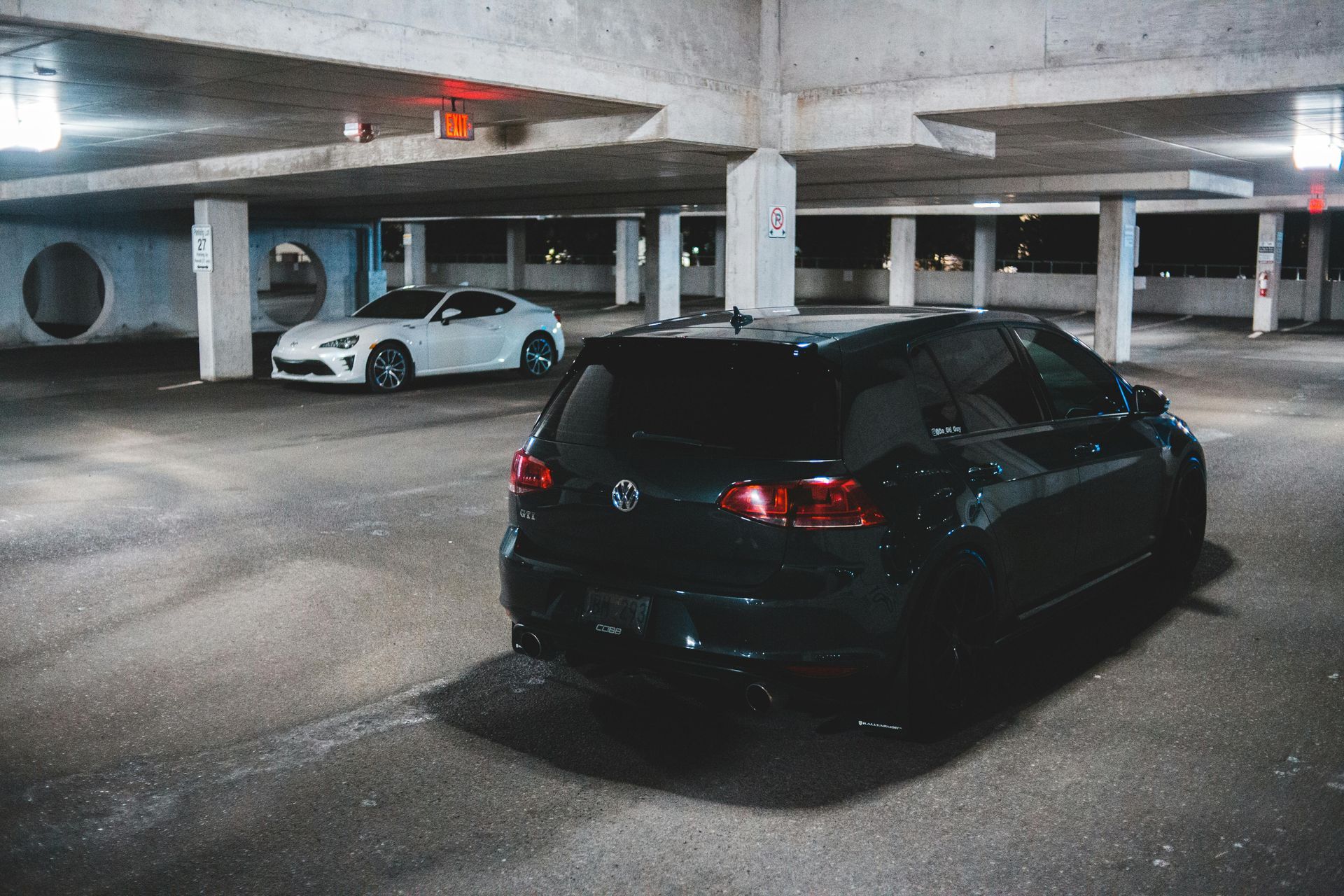 Black Volkswagen Golf R parked in a dim parking garage; a white sports car is in the background.