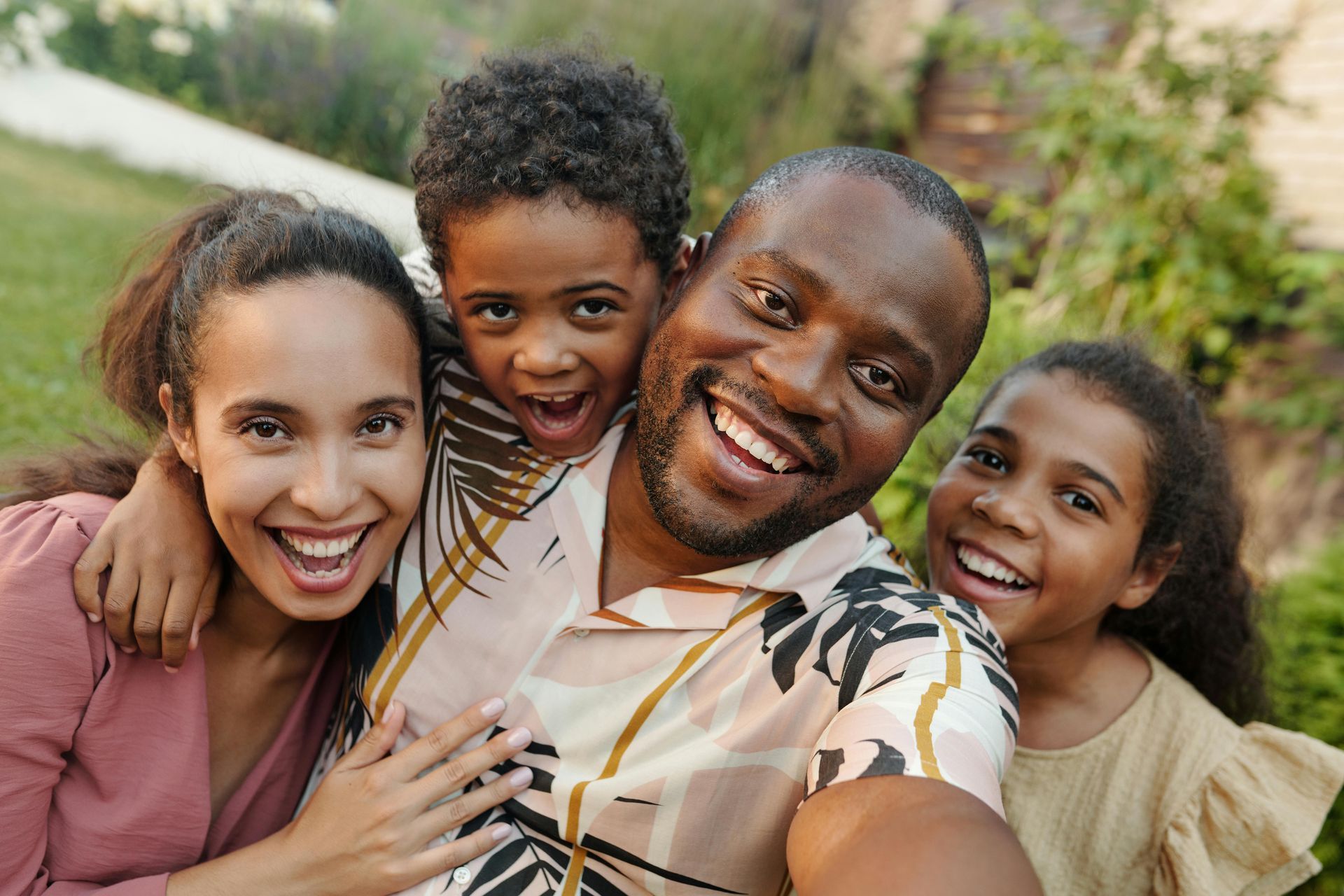 Family portrait: smiling parents and children in a garden, embracing and looking at the camera.