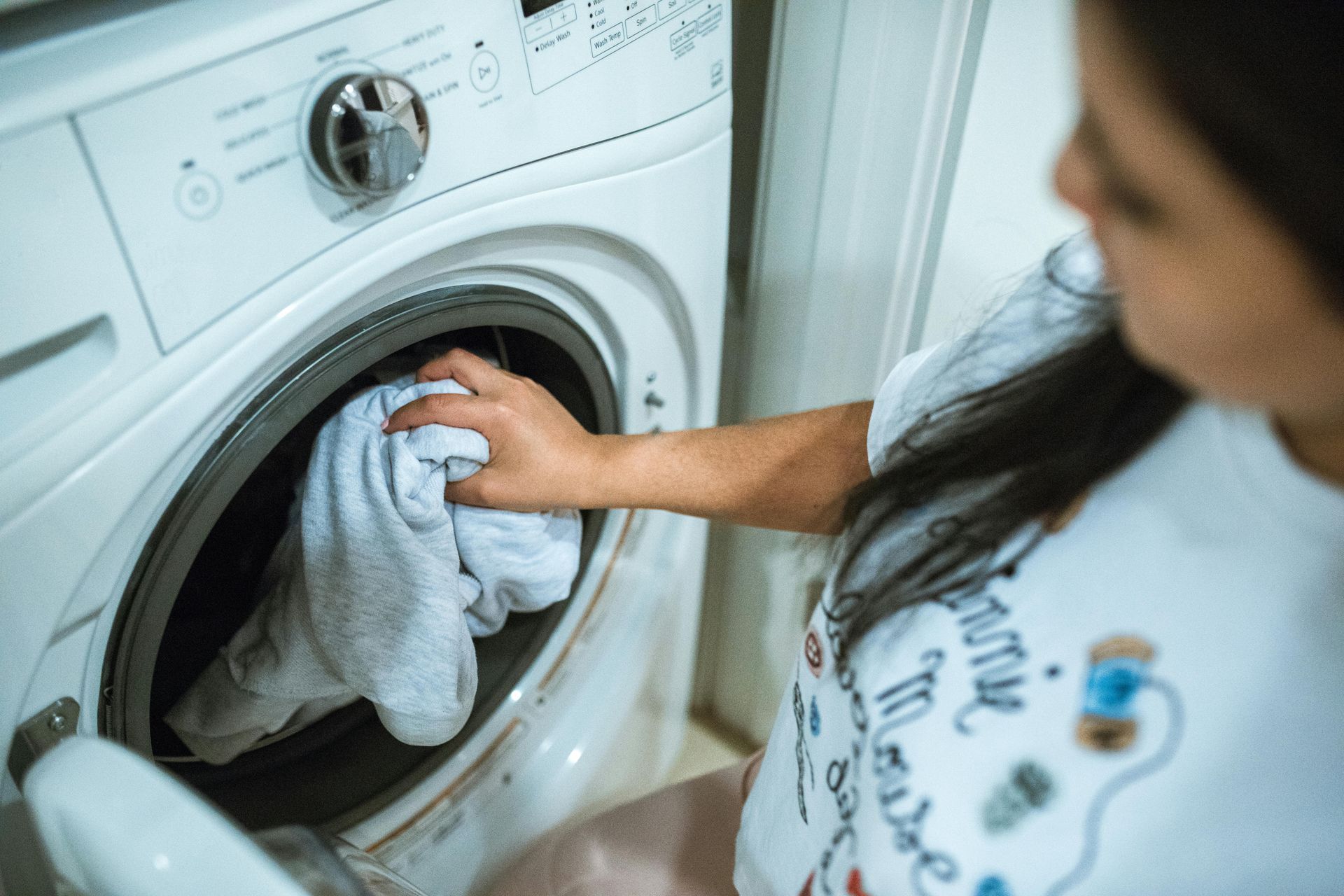 Woman loading white clothes into a washing machine in a laundry room.