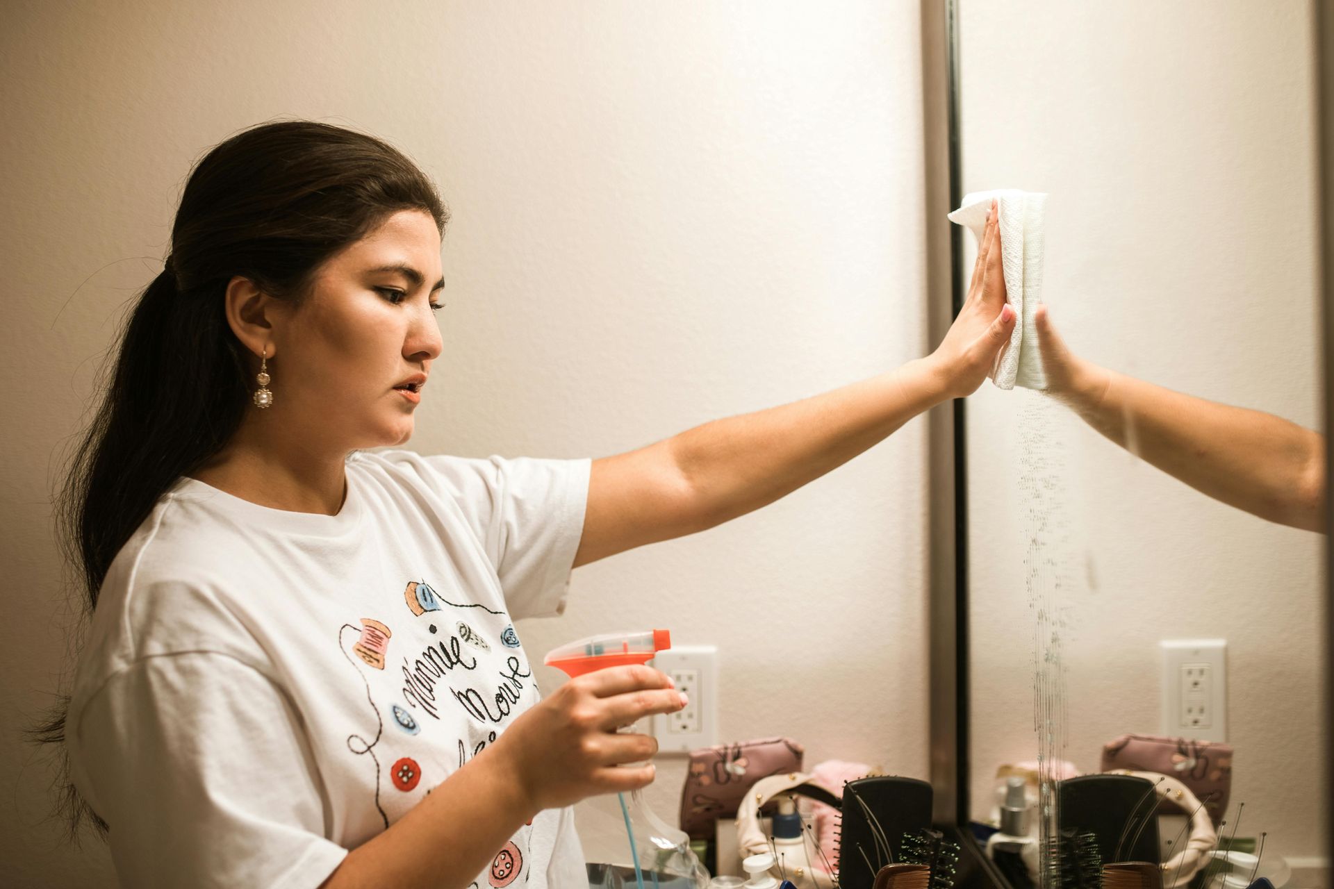 Woman cleaning a mirror with spray and cloth in a bathroom.