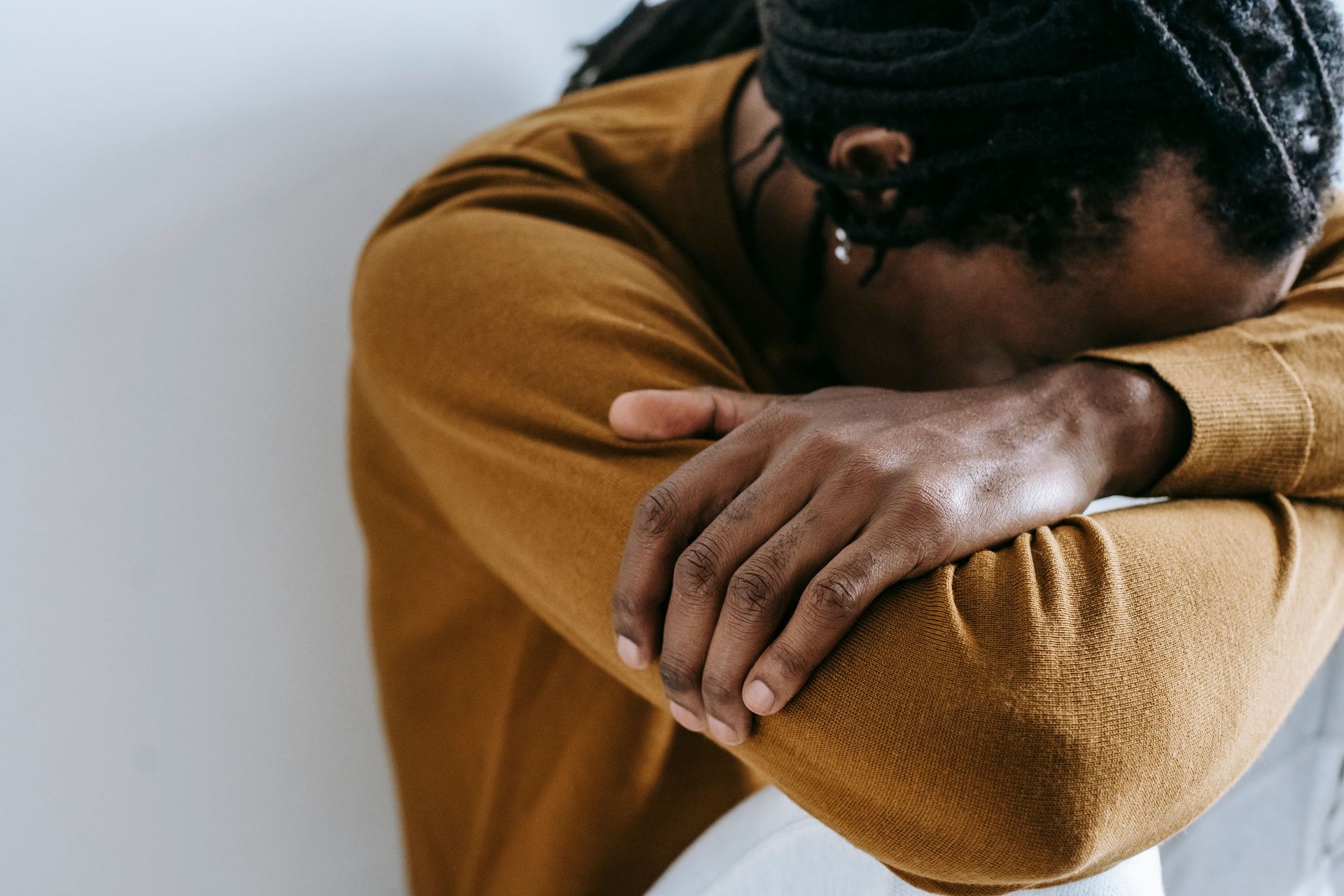Person in a mustard sweater rests their head on folded arms, appearing upset.