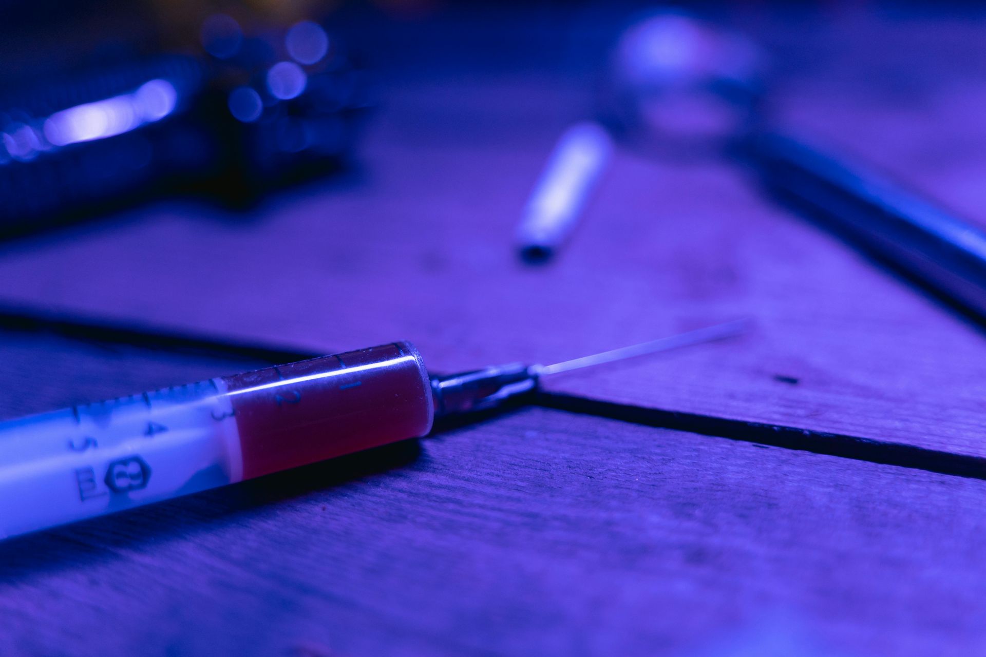 Hope Against Trafficking / A syringe filled with red liquid is sitting on a wooden table.