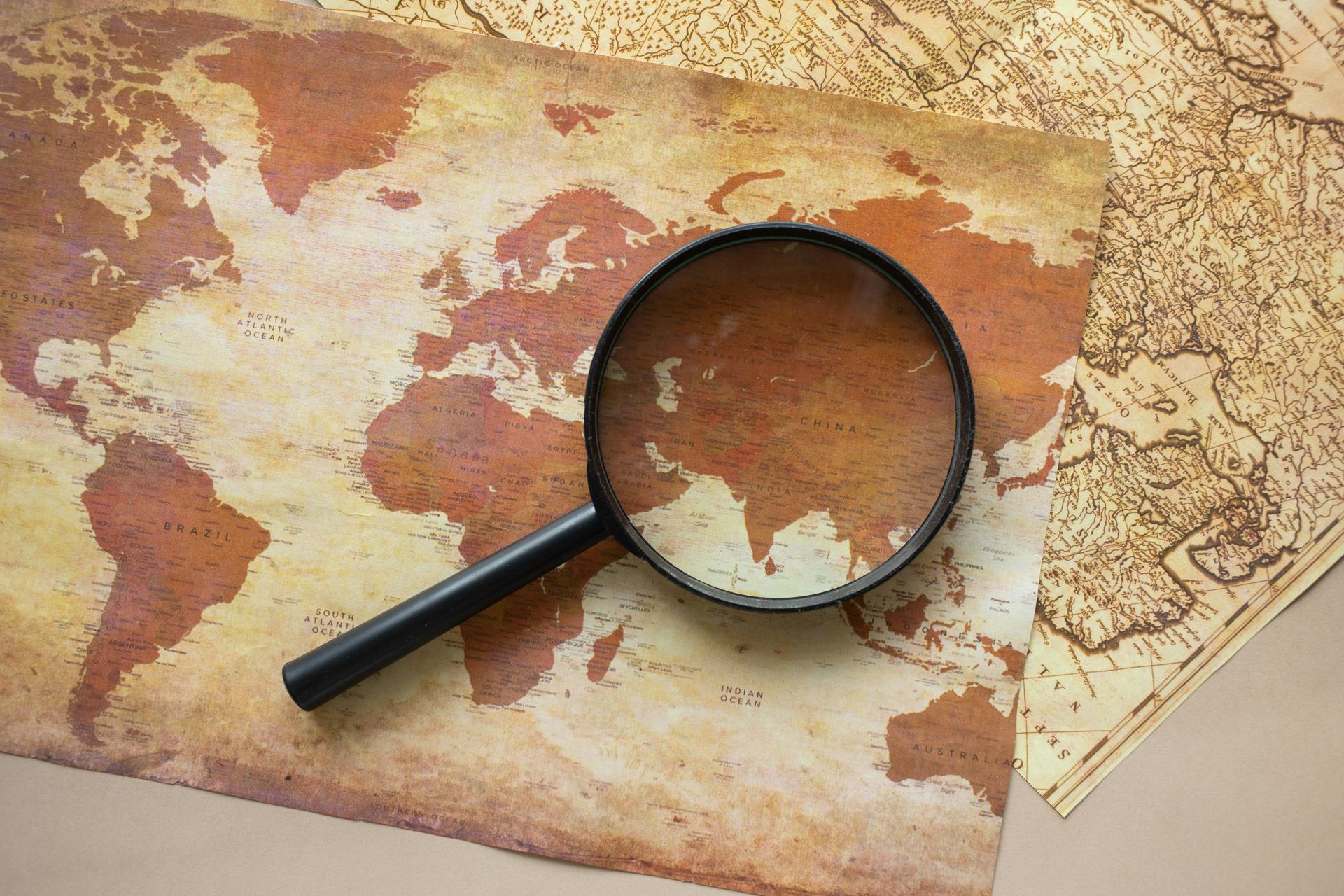 Magnifying glass on an old, sepia-toned map with a folded paper map beneath it