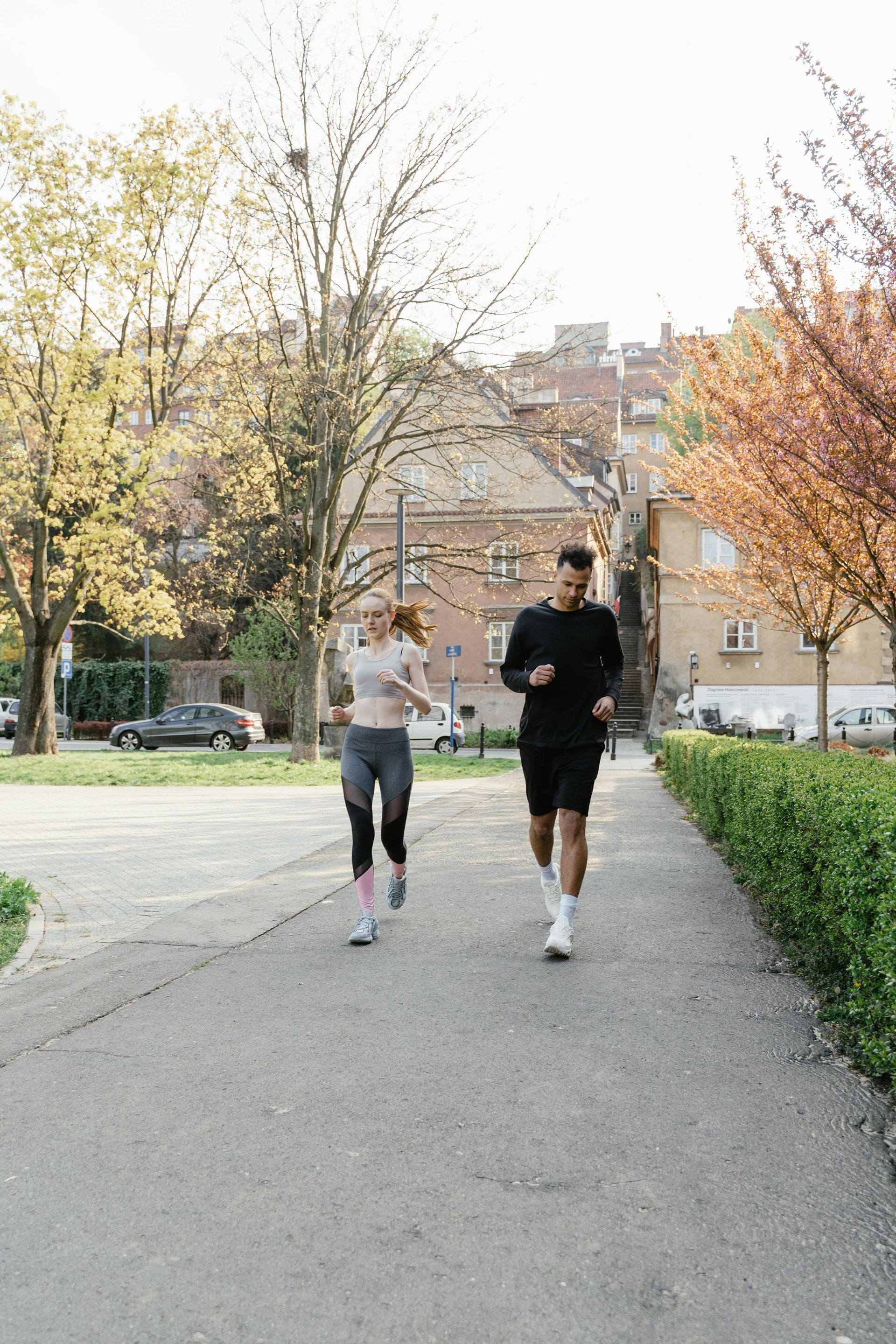 A man and a woman are jogging on a path in a park.