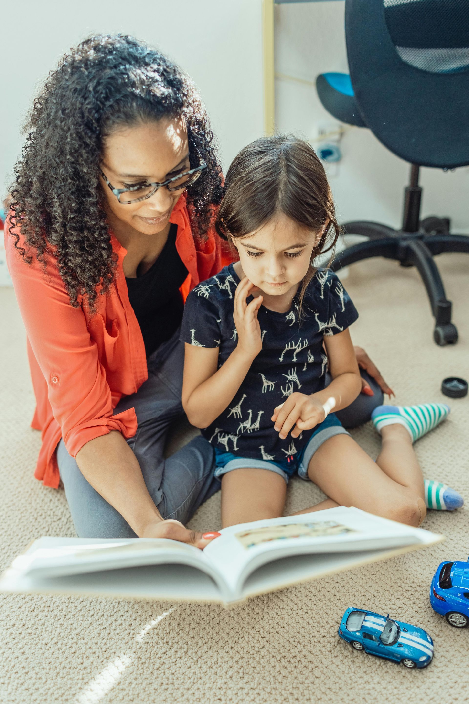 A woman is sitting on the floor reading a book to a little girl.