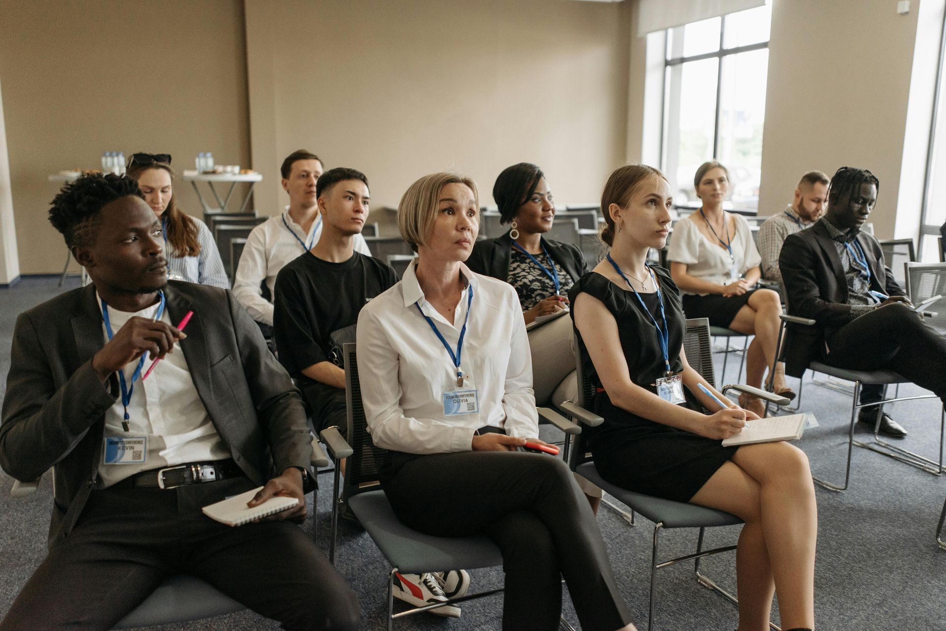 People seated in chairs, attending a conference, with notepads and pens.