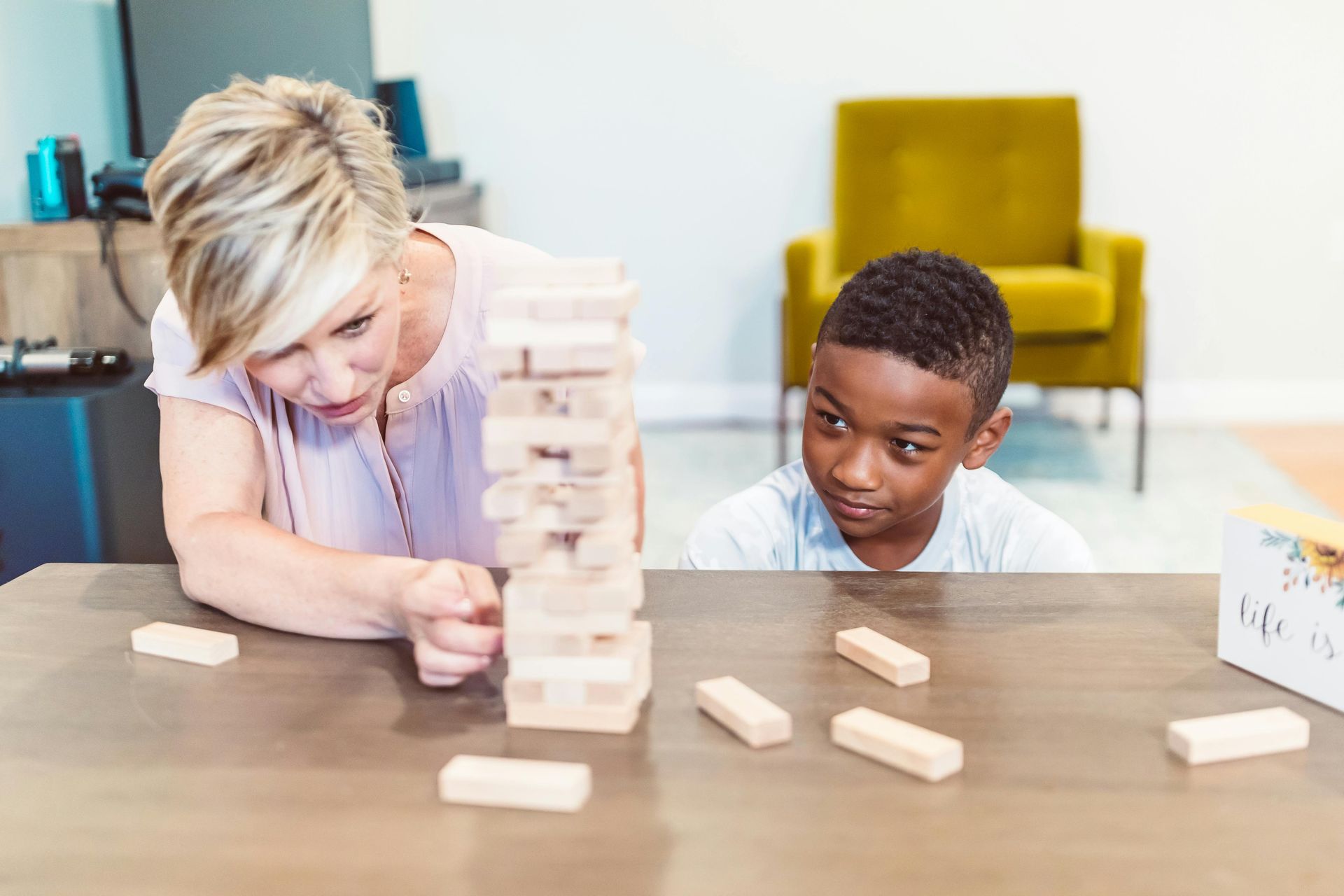 A woman and a boy are playing jenga at a table.