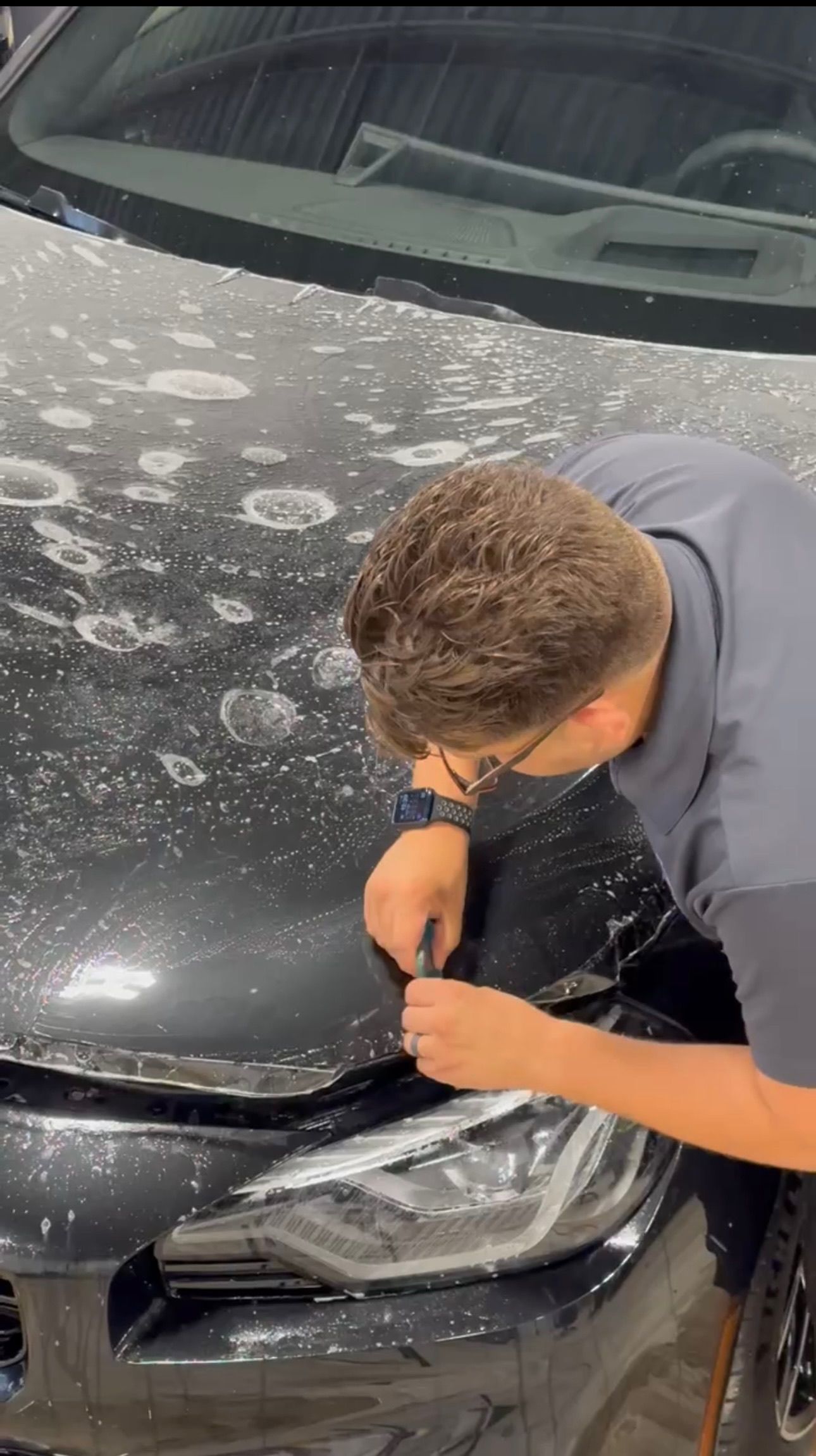 a man is applying a protective film to the hood of a car .