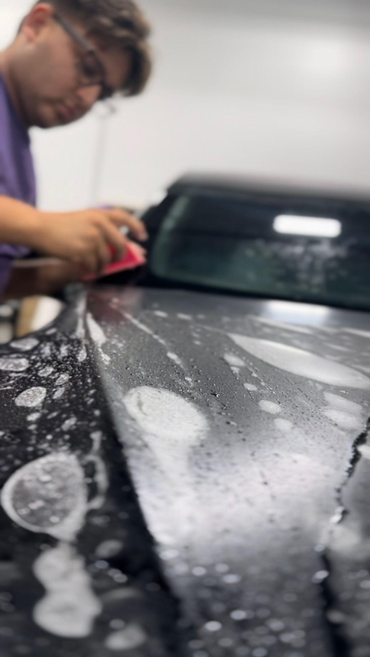 a man is cleaning the hood of a car with a cloth .
