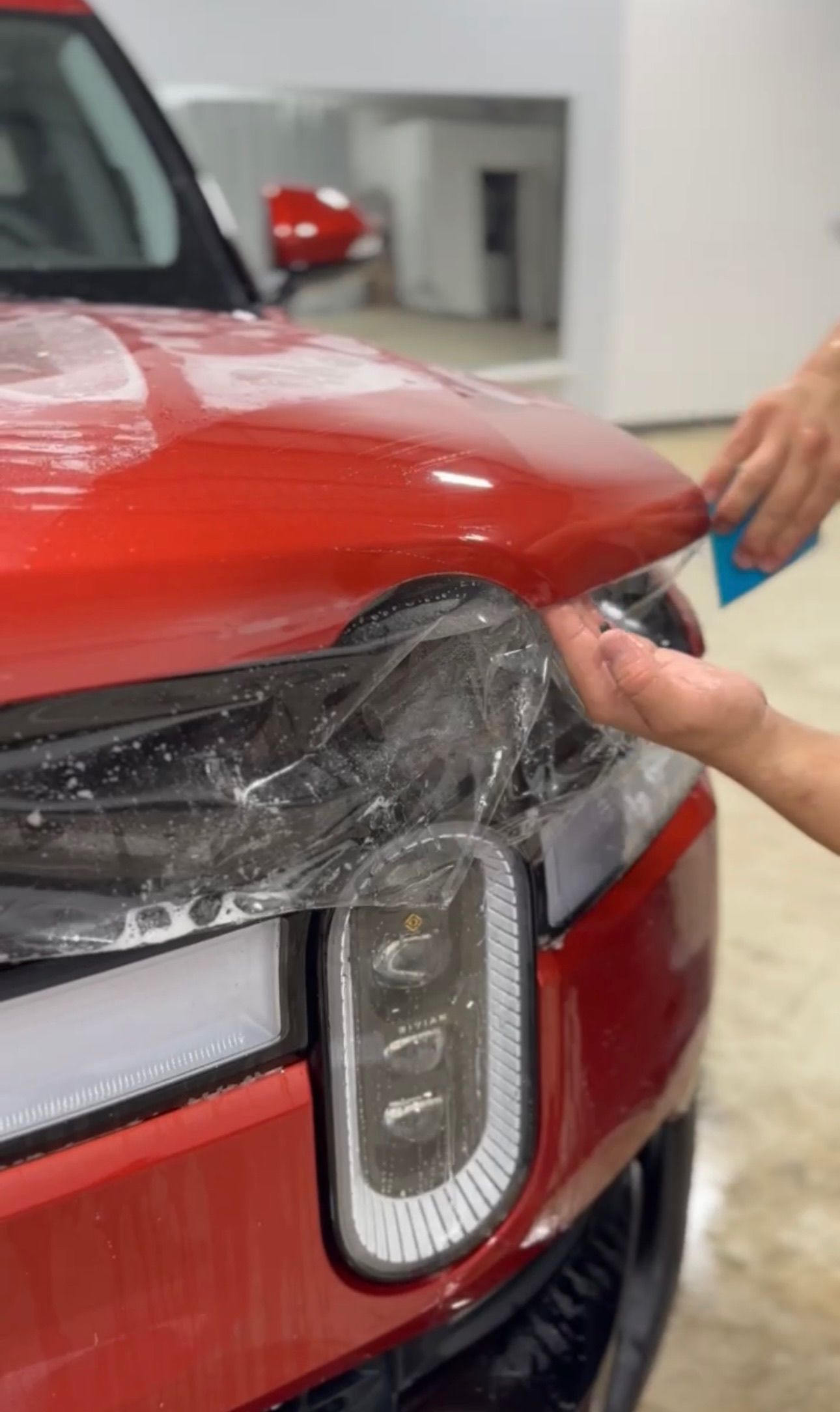 a person is applying a protective film to the headlights of a red car .