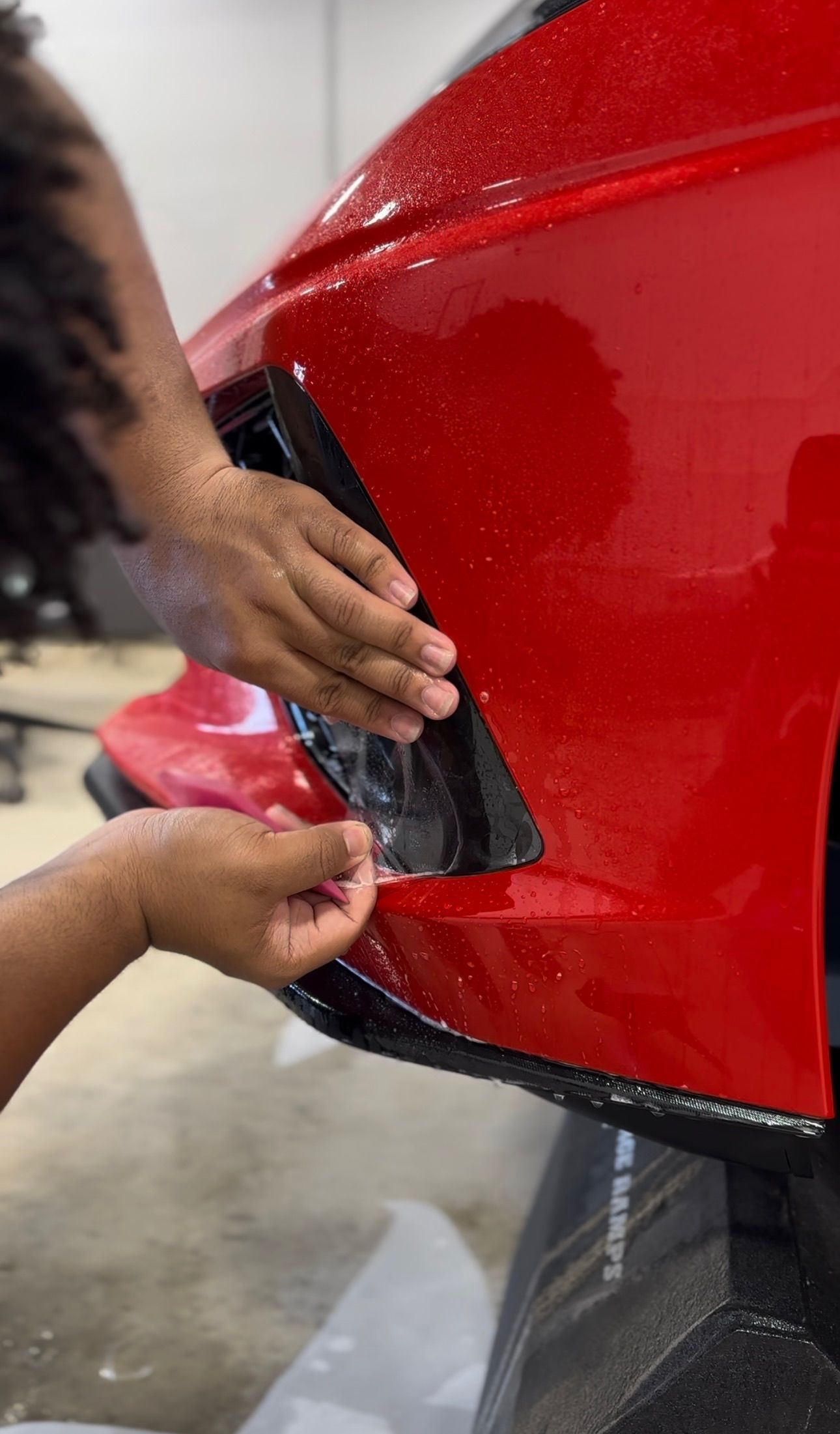 a person is applying a protective film to the front bumper of a red car .