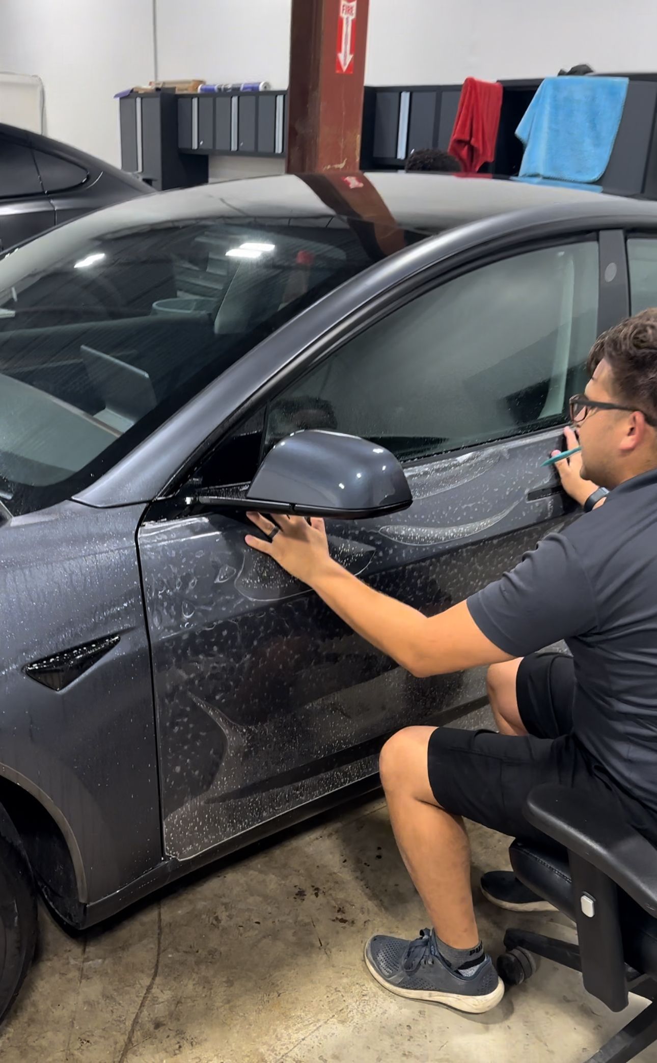 Man applying film to a grey car door in a garage.
